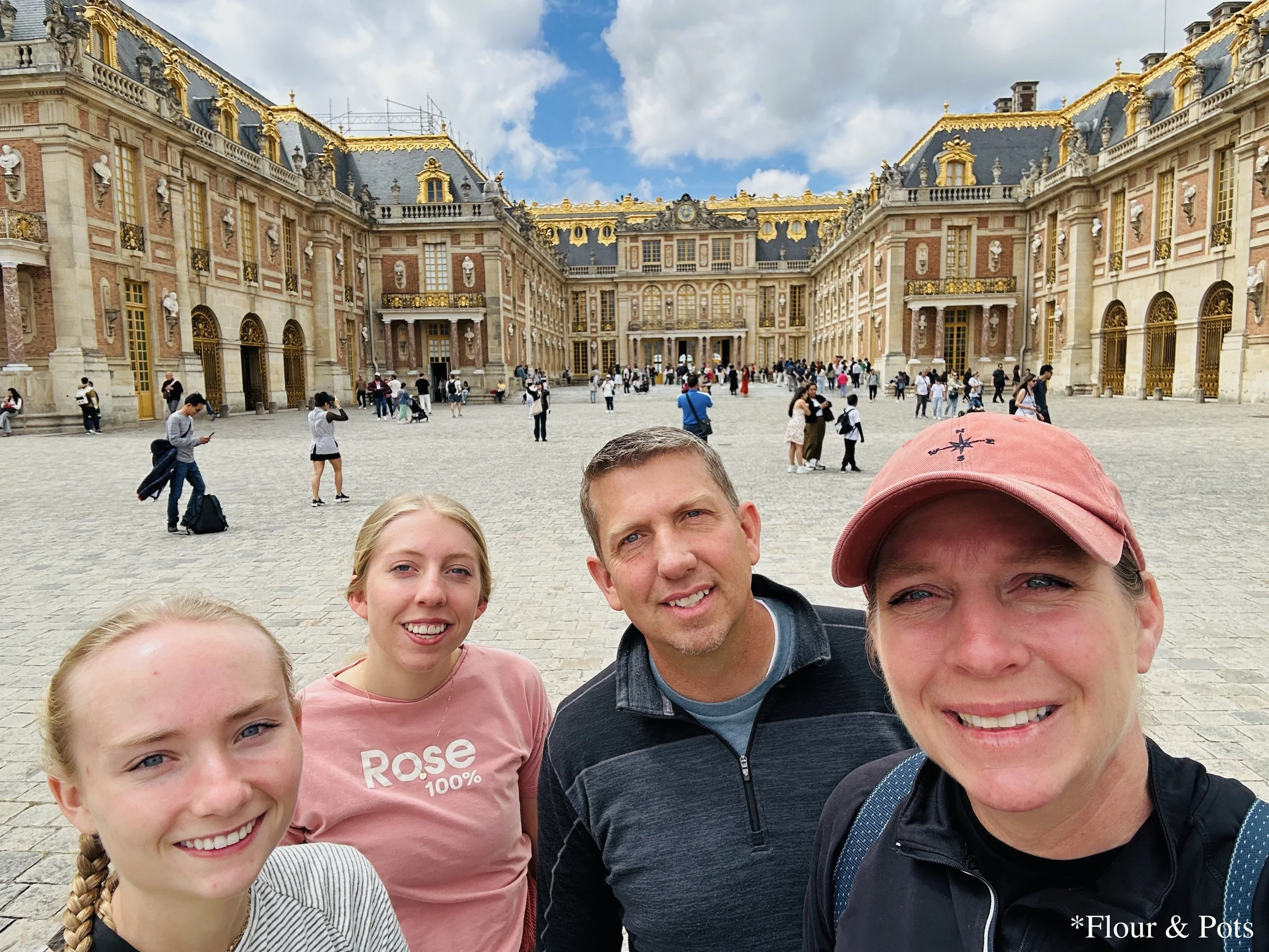 Family selfie taken in front of the golden entrance of the Palace of Versailles, Paris.