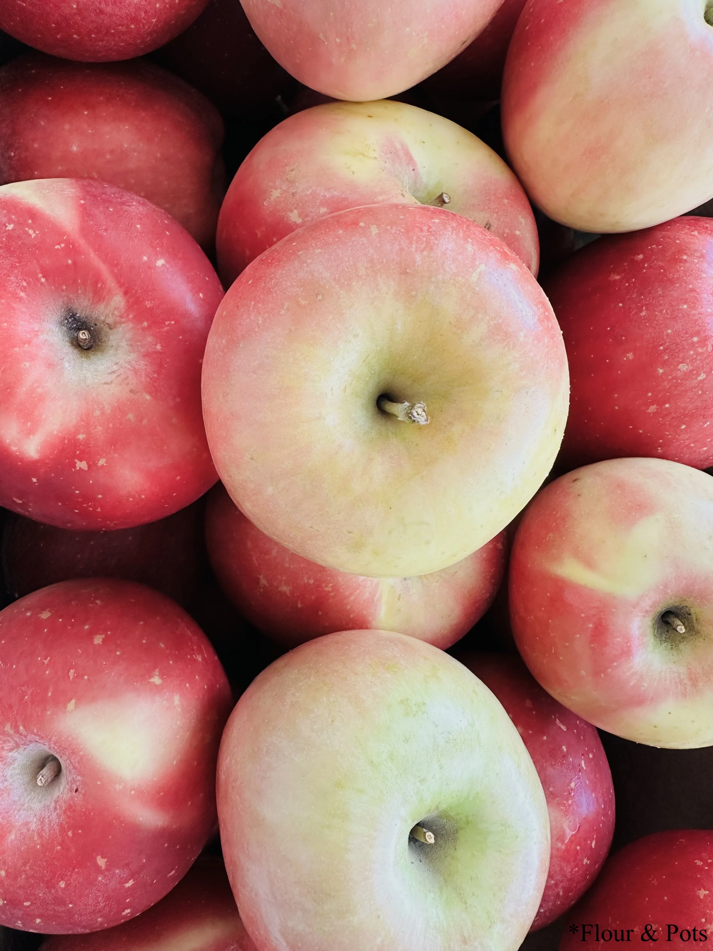 Overflowing fresh Fuji apples in a box from a local fruit stand, showcasing their vibrant red and yellow hues.