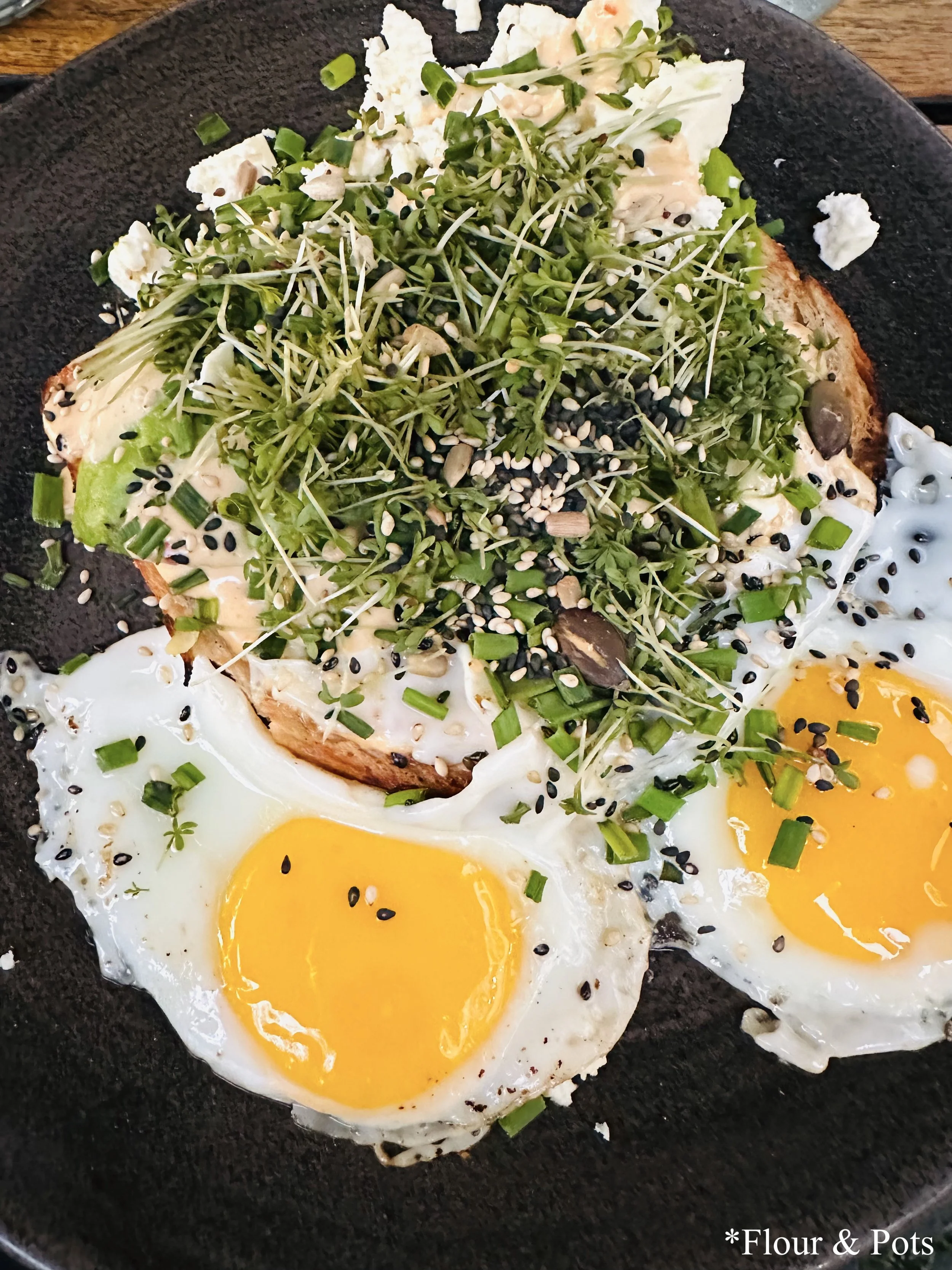 Avocado toast from Cotidiano in Munich, Germany, featuring toasted sourdough bread topped with avocado, tomato salsa, two fried organic eggs, mixed seeds, and herder’s cheese.