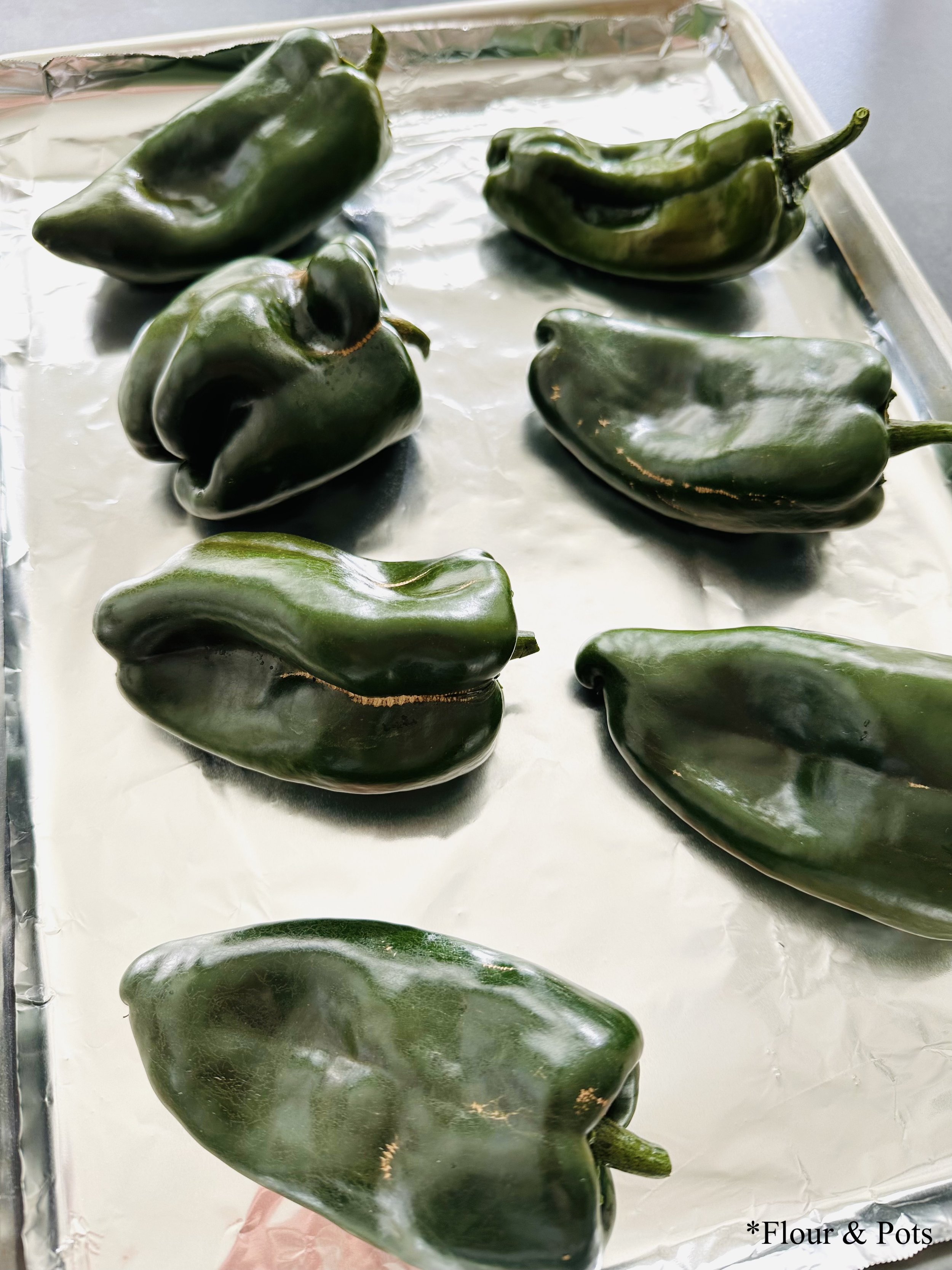 Fresh poblano peppers on a sheet pan lined with foil, prepared for roasting in the oven.
