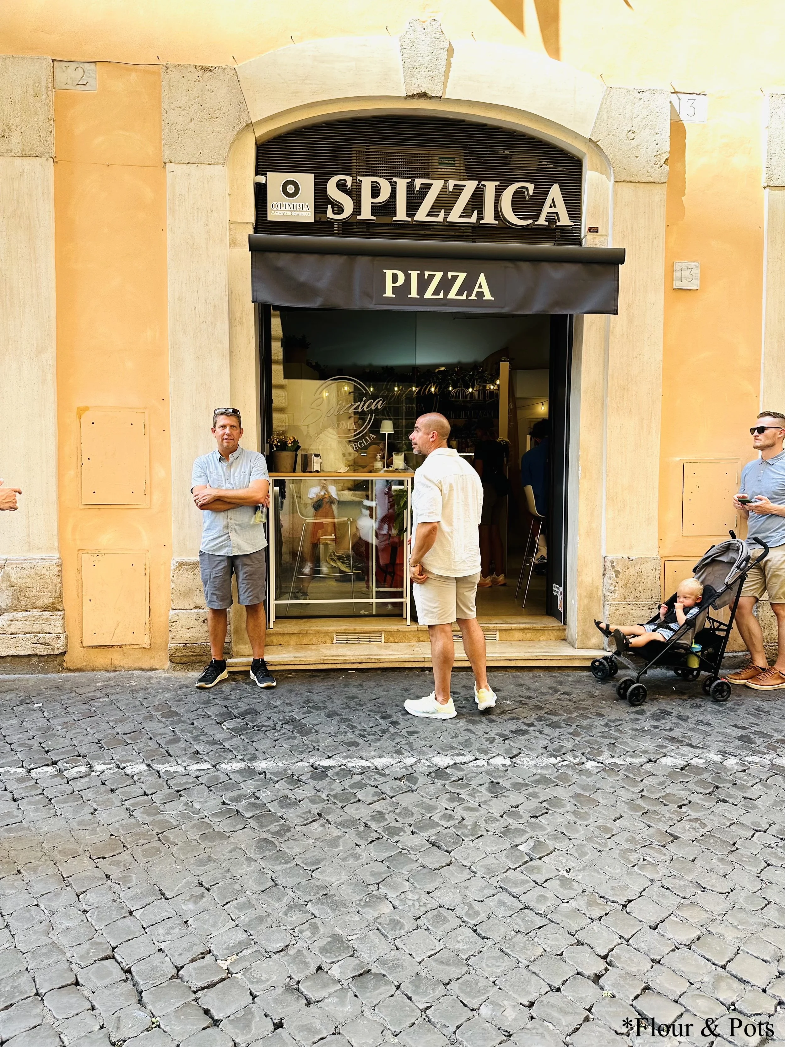 Exterior storefront of Spizzica Roma, a popular pizza spot in Rome, Italy, with a welcoming entrance and signage.