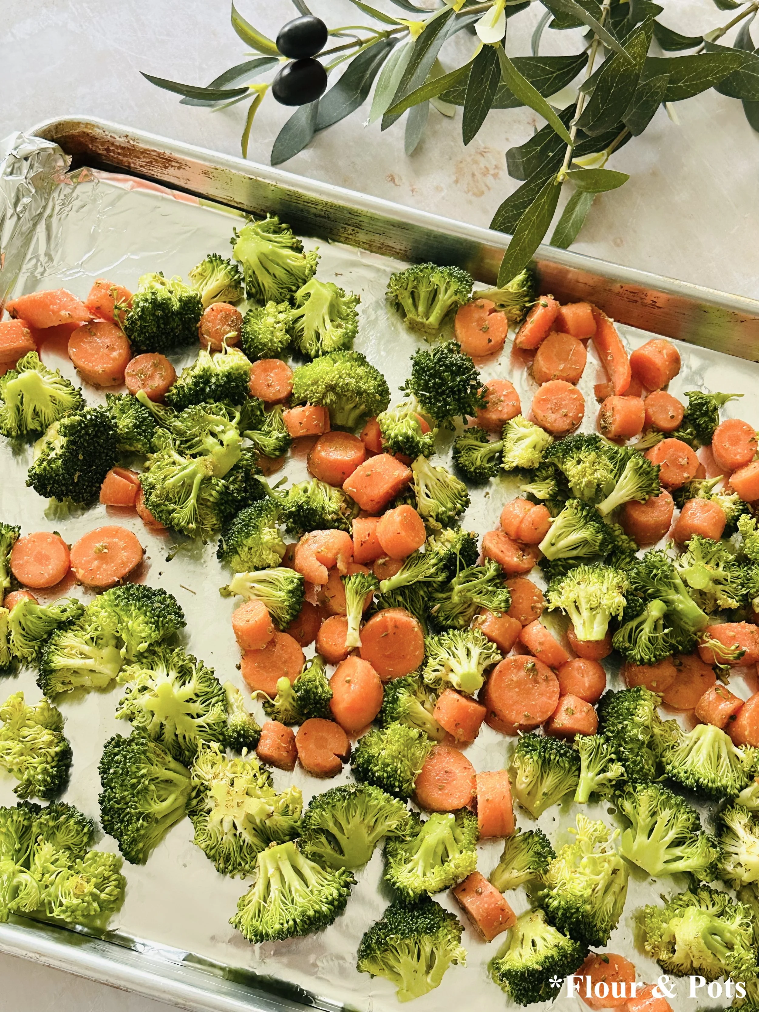Roasted broccoli and carrots on a baking sheet before assembling salad.