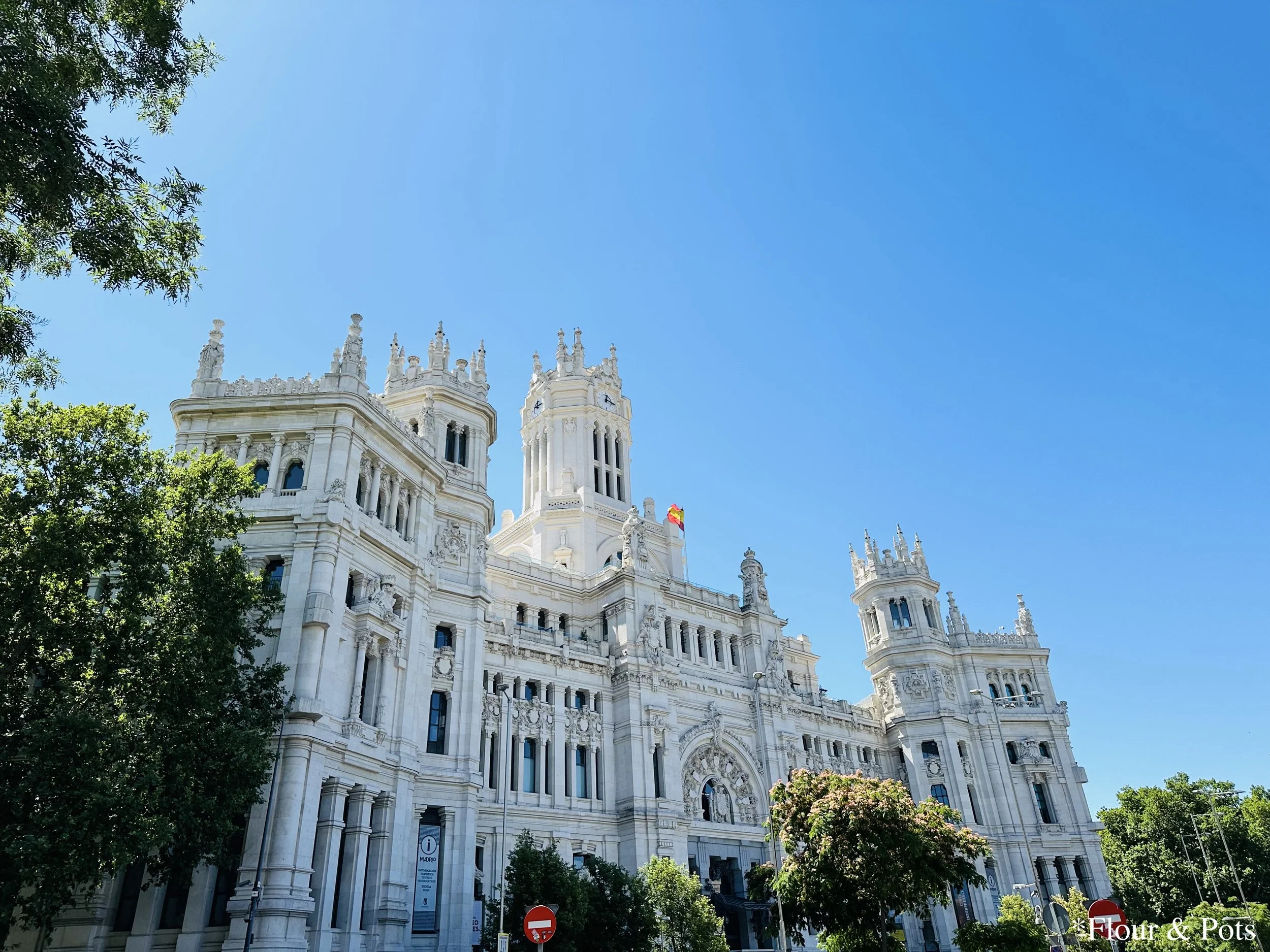 The historic Old Post Office building in Madrid, Spain, with a vibrant blue sky in the background and the Spanish flag proudly flying.