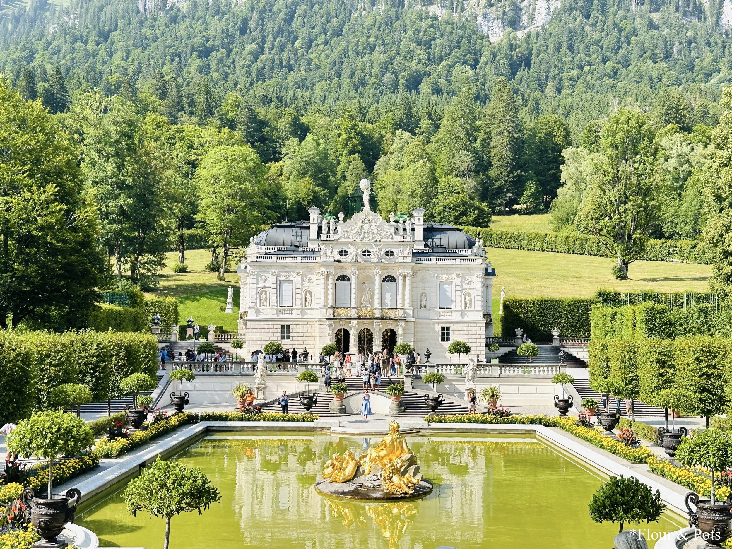 Linderhof Palace entrance, with its intricate facade surrounded by lush greenery and gardens in Bavaria.