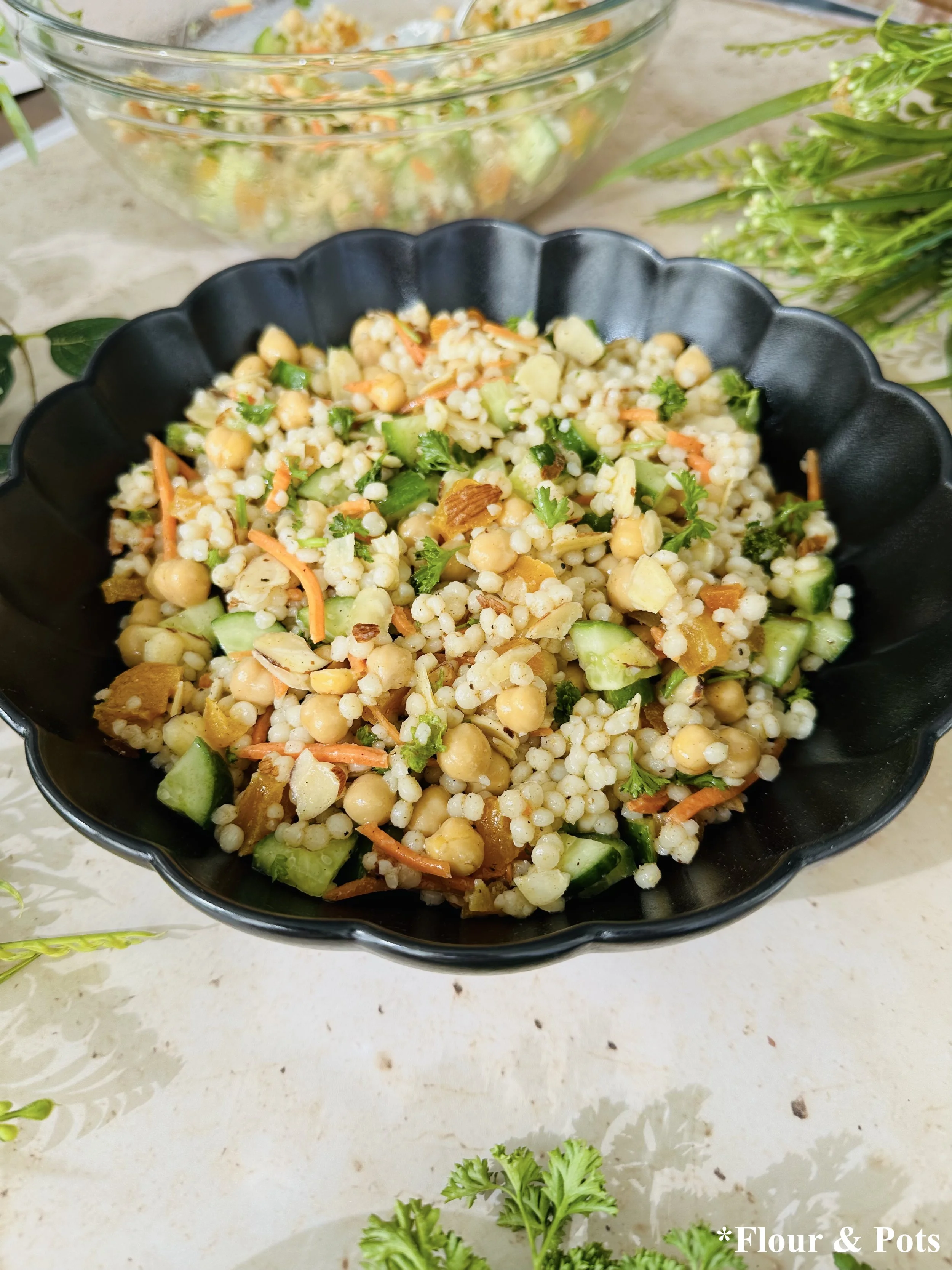 Bowl of Moroccan-inspired couscous salad with chickpeas, cucumbers, apricots, and almonds, drizzled with lemon spice dressing