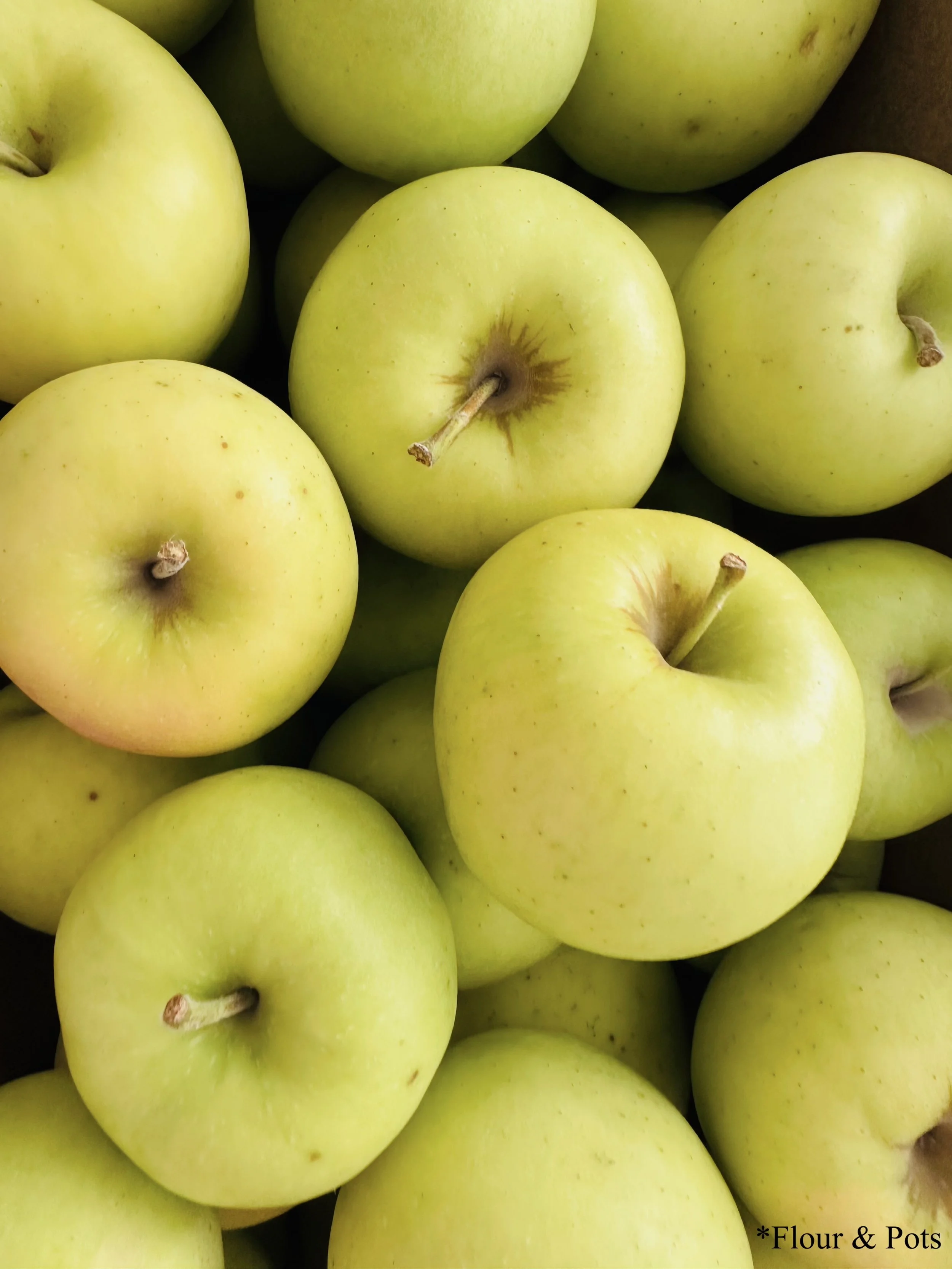 Golden Delicious apples neatly packed in a fruit box at a local fruit stand, featuring their golden-yellow skin.