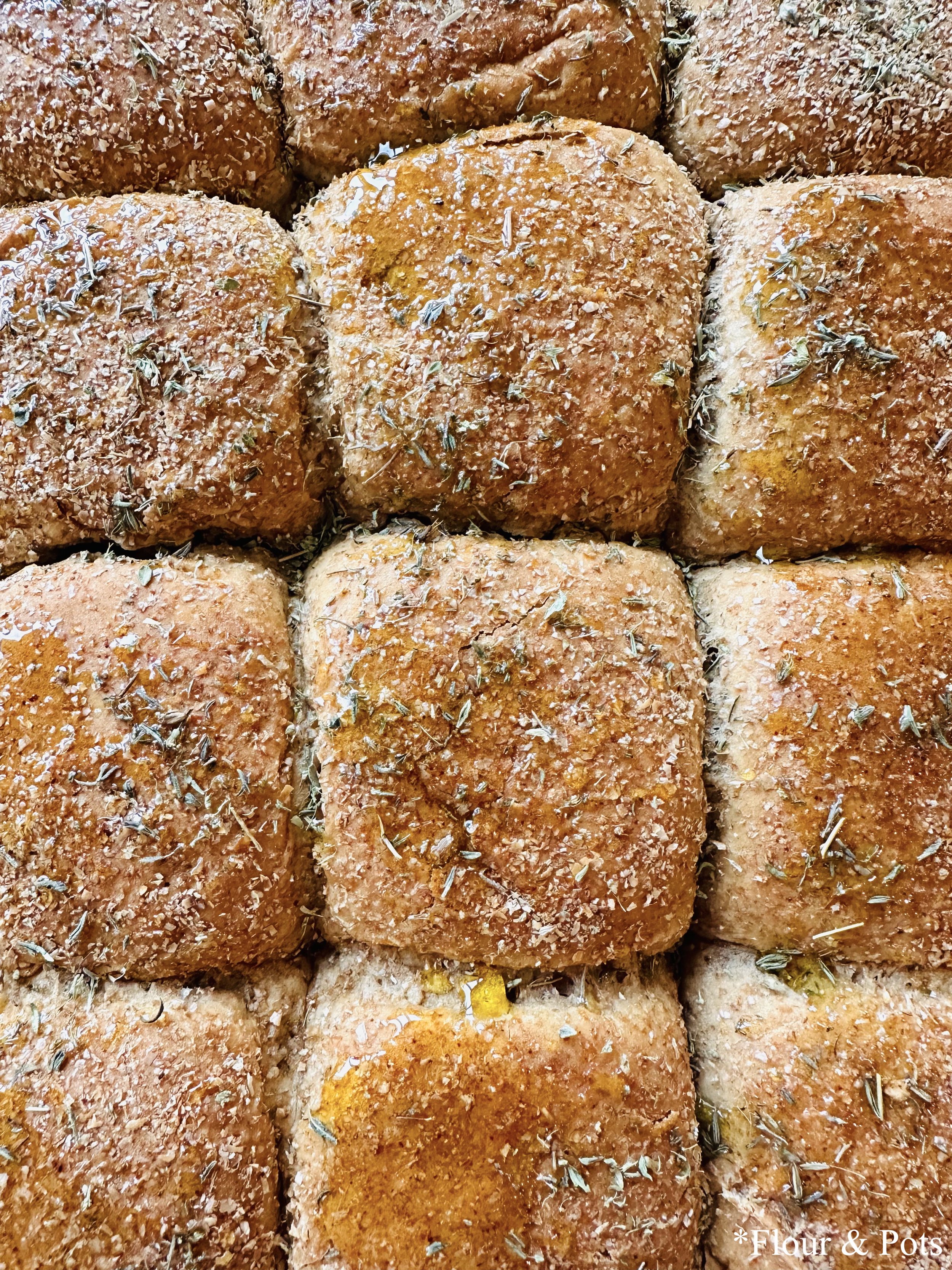 Close-up of small chicken sliders topped with thyme and olive oil, featuring a golden, herby baked crust. The sliders are served on soft, lightly toasted buns, garnished with fresh herbs for added flavor and visual appeal.