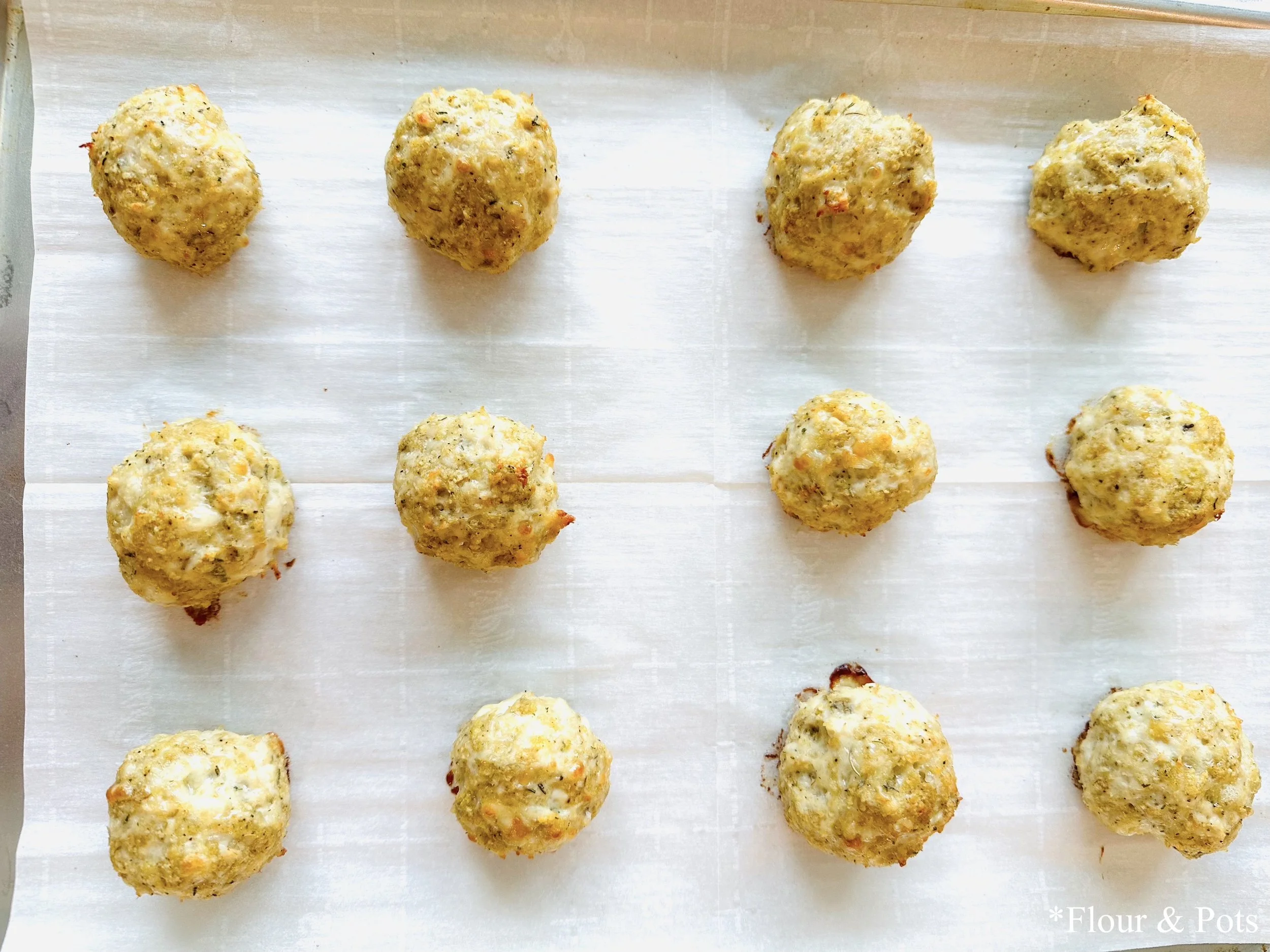 Close-up of baked chicken meatballs seasoned with herbs on a baking sheet.