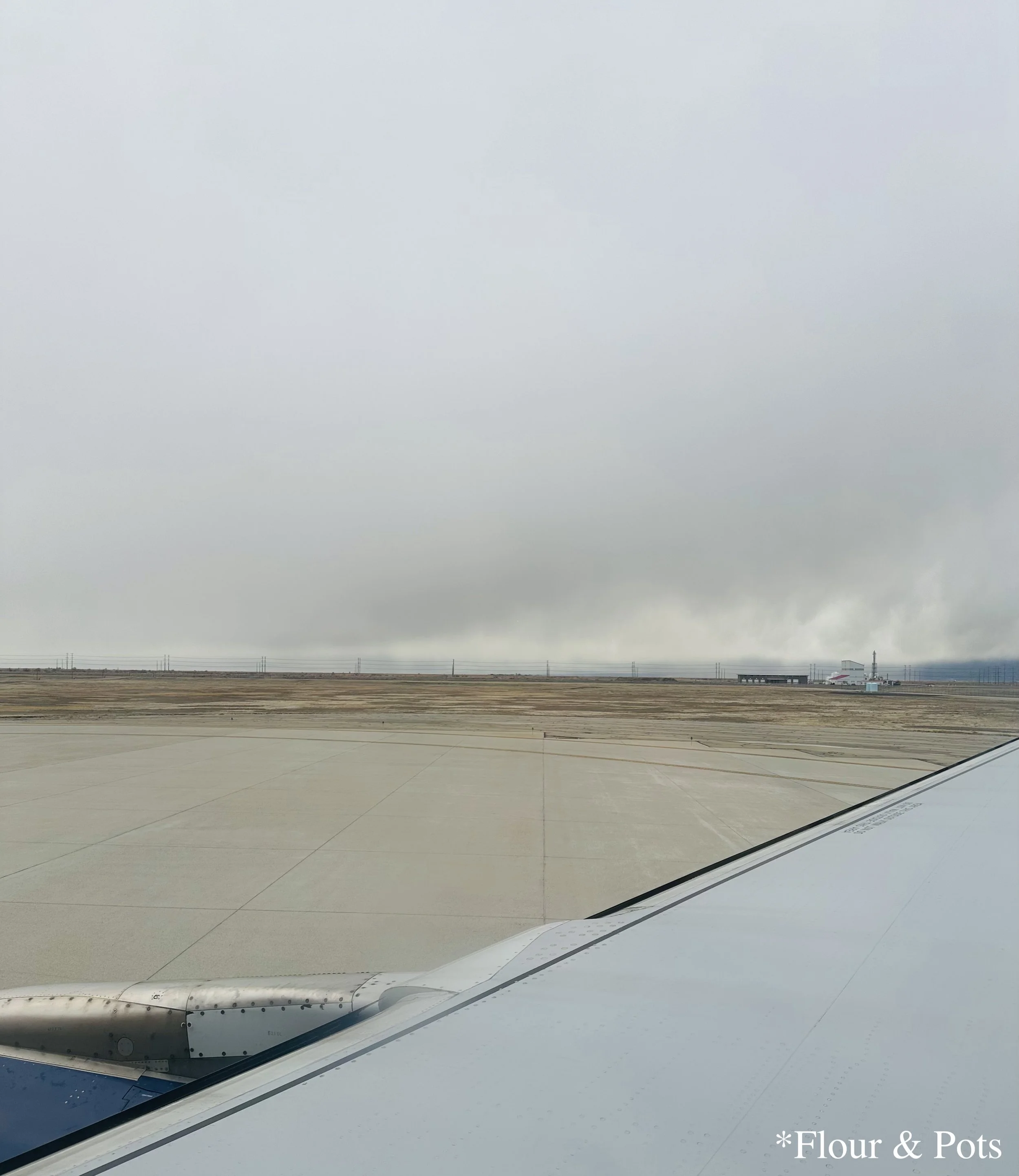 View from an airplane window during a flight from Salt Lake City to Orlando, Florida, on a stormy March day. Dark clouds and patches of rain cover the sky, with glimpses of the landscape far off.