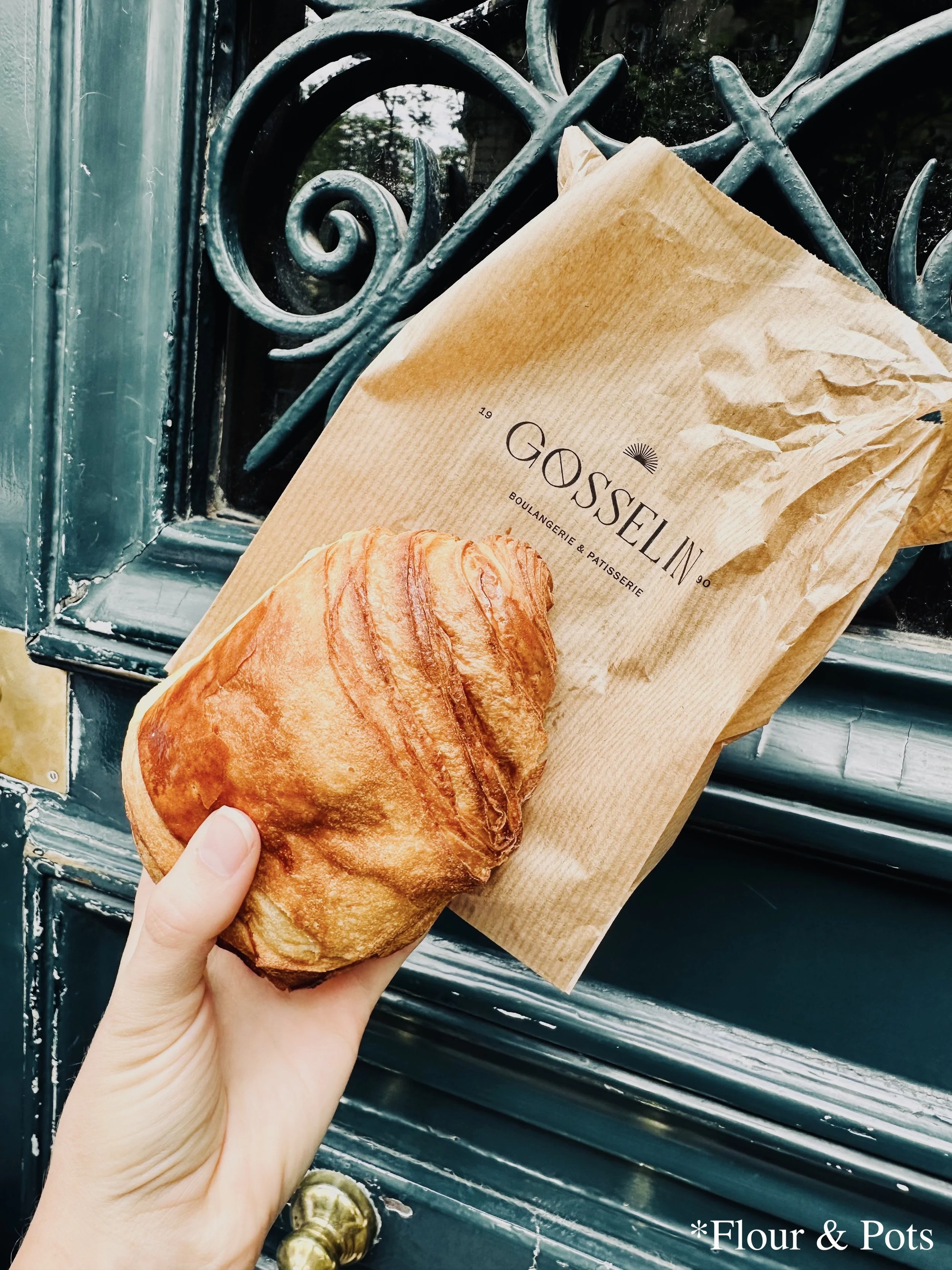 A Pain au chocolat from Gosselin bakery is held up in front of an old green-blue door in Paris, France.