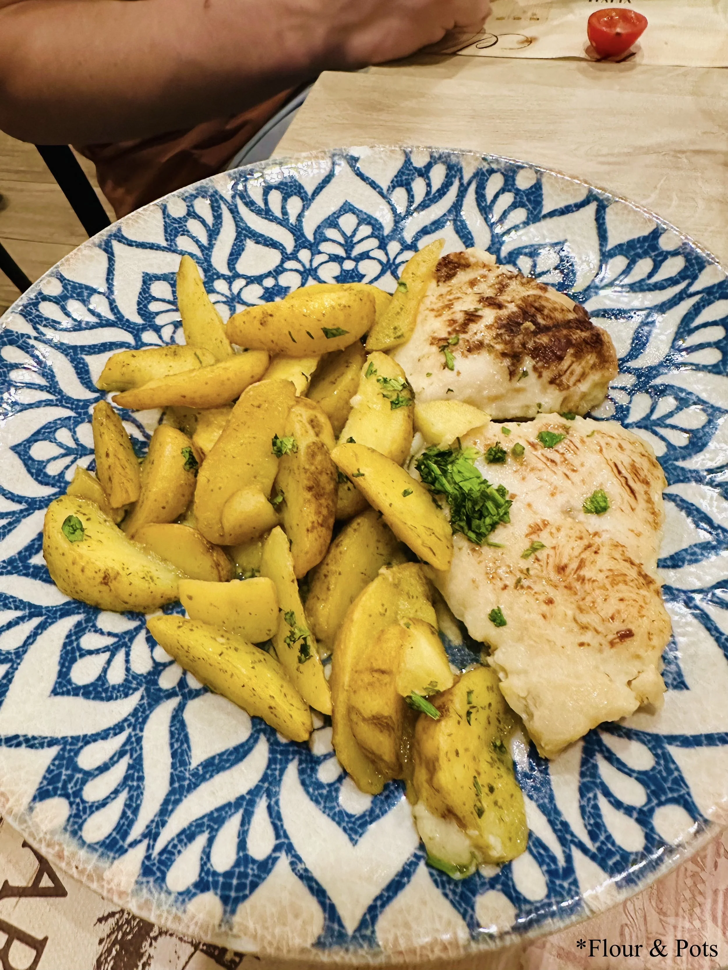Chicken and potatoes served on a blue tile-style plate at La Panetteria in Rome, Italy.