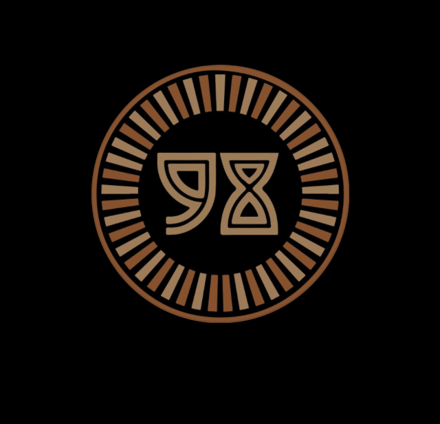 A circular logo with a black background and a bronze border, featuring abstract symbols in the center.