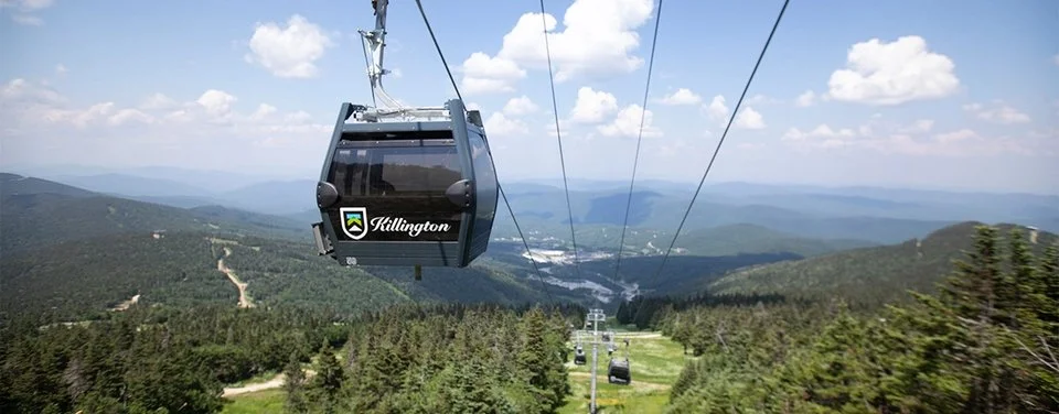 Cable car traveling above a lush, green mountain landscape with blue sky and scattered clouds.