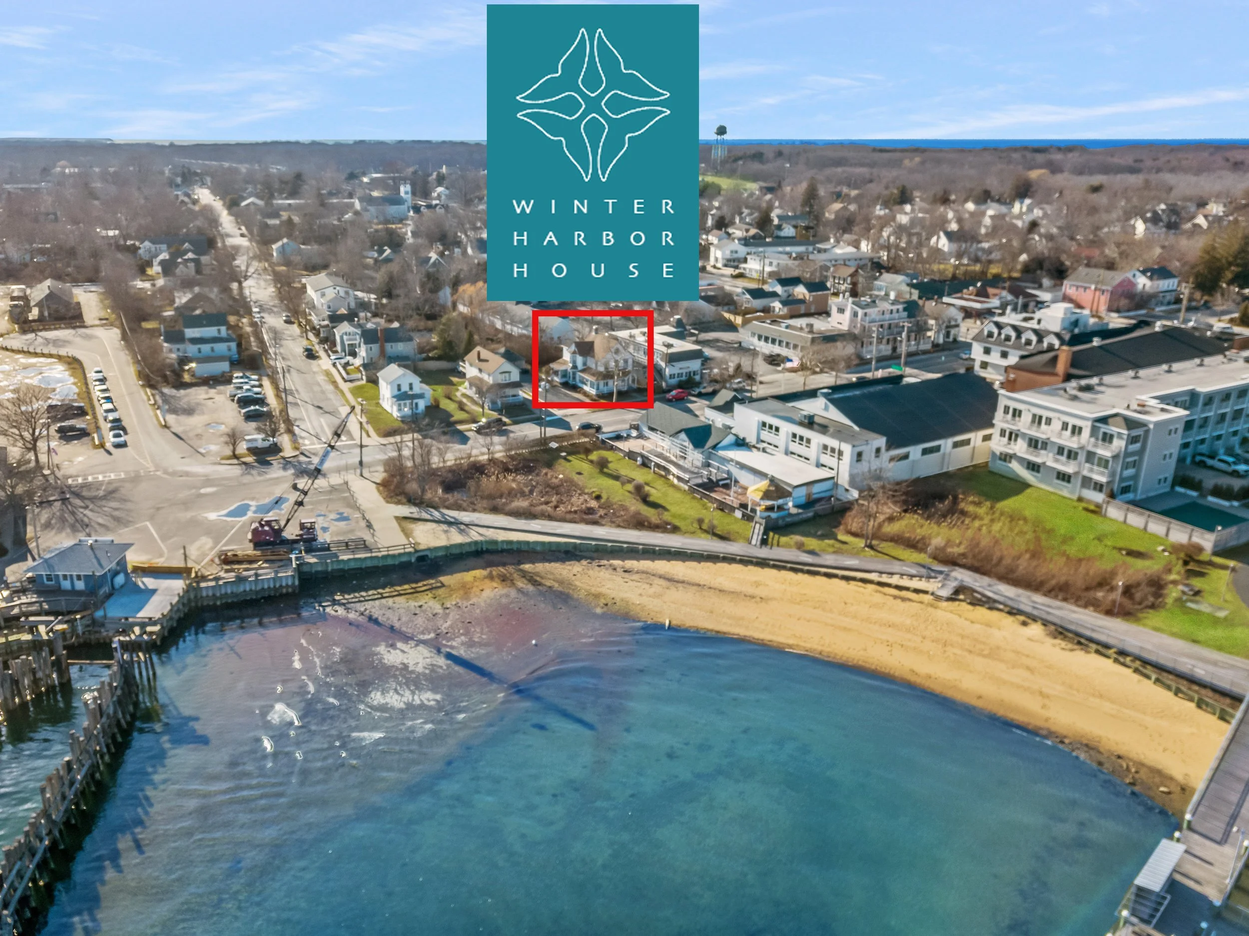 Aerial view of a coastal neighborhood with a beach, a pier, and houses along the shoreline. The image features a logo for Winter Harbor House at the top.