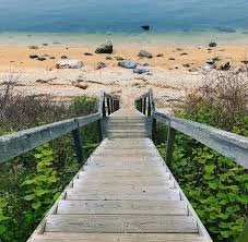 Wooden pier leading to a sandy beach and clear blue water.