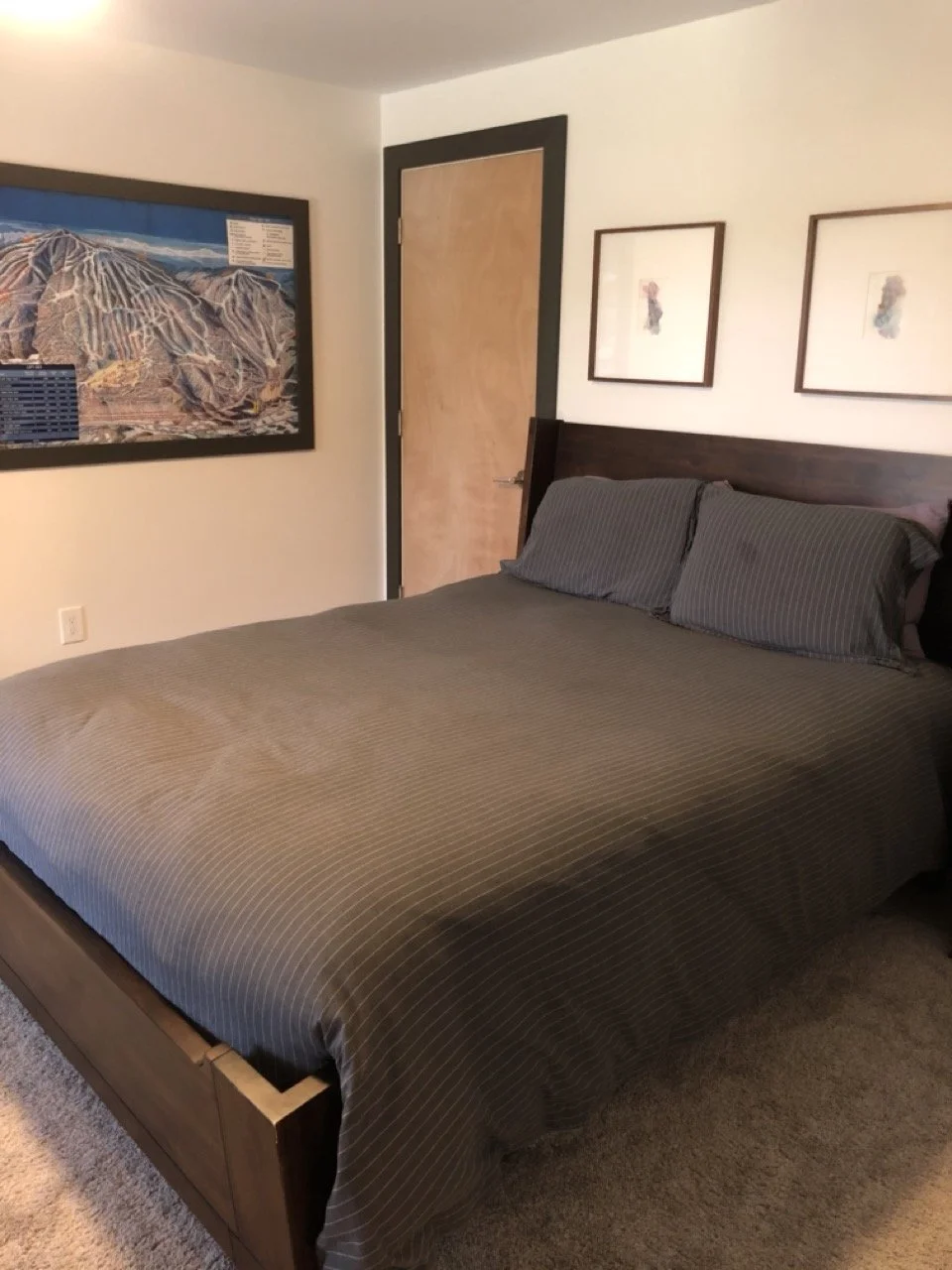 A neatly made bed with dark gray striped bedding and matching pillows in a room with framed art and a landscape picture on the wall.