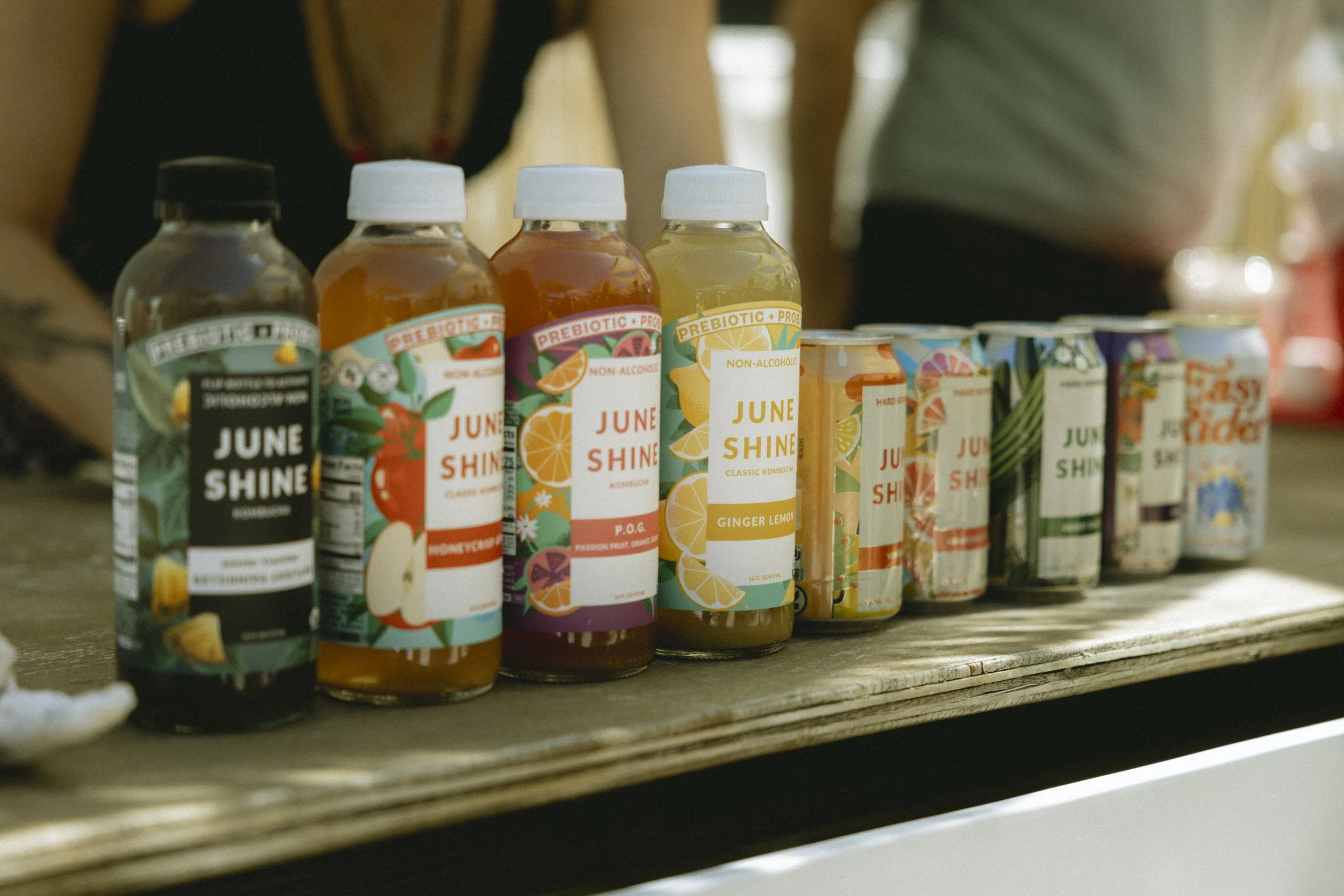 A variety of bottled beverages with colorful labels, including juices and kombucha, displayed on a wooden surface.