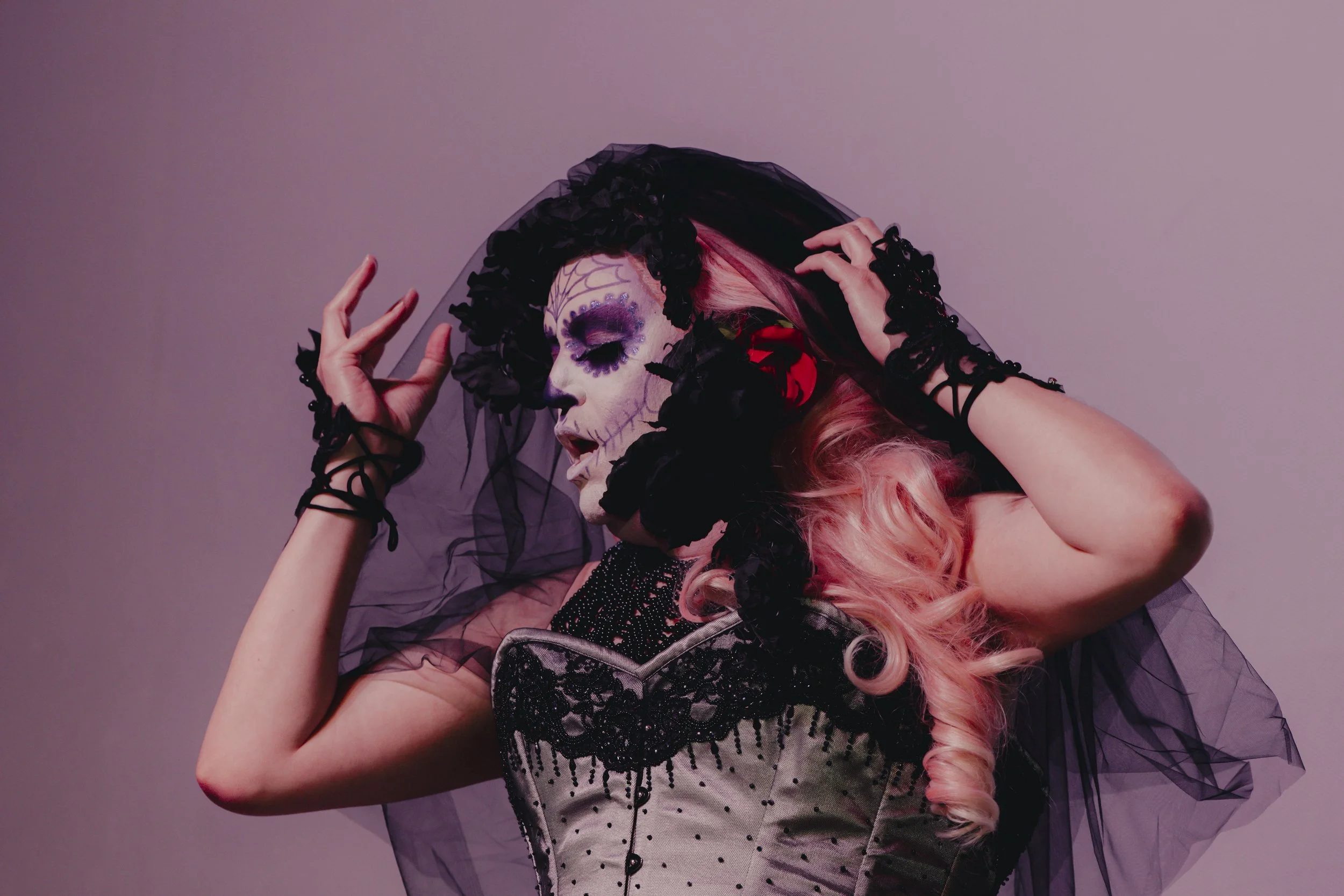 Woman in Day of the Dead makeup with pink hair, wearing a black veil and vintage dress, and black lace gloves.