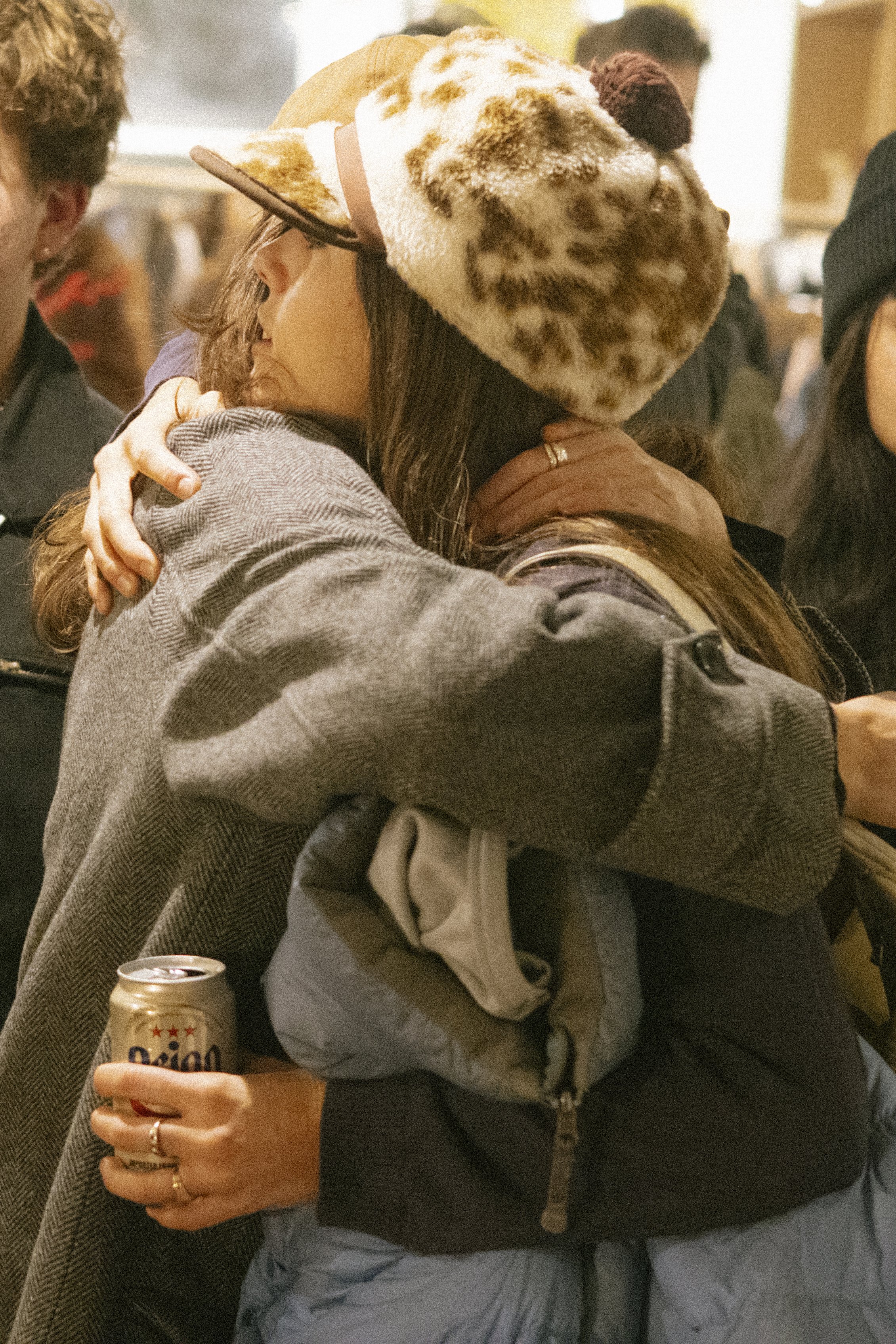 People hugging in a social gathering, with one person holding a can of Oznion soda.