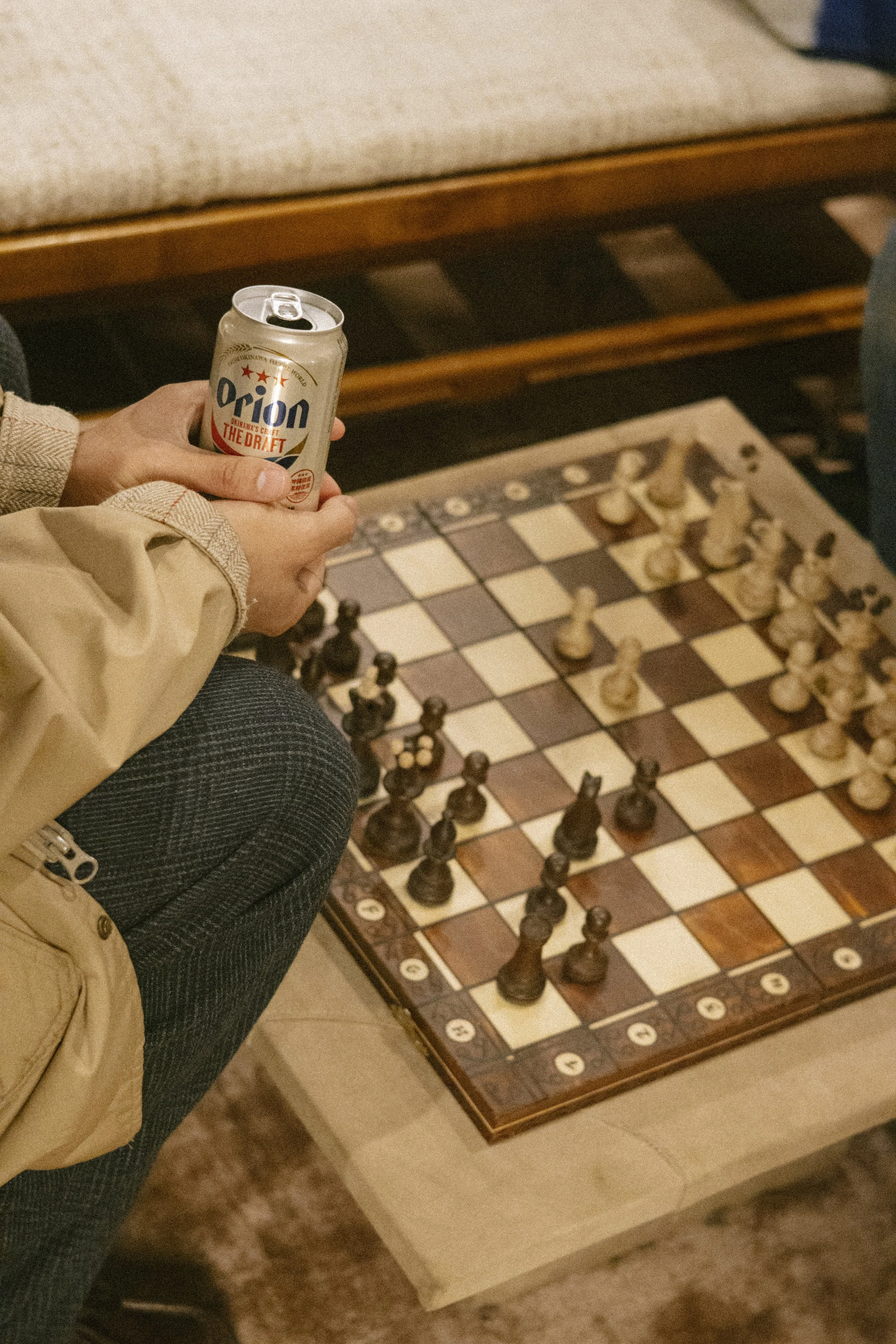 Person holding a can of Orion beer while sitting near a chessboard set up for a game.