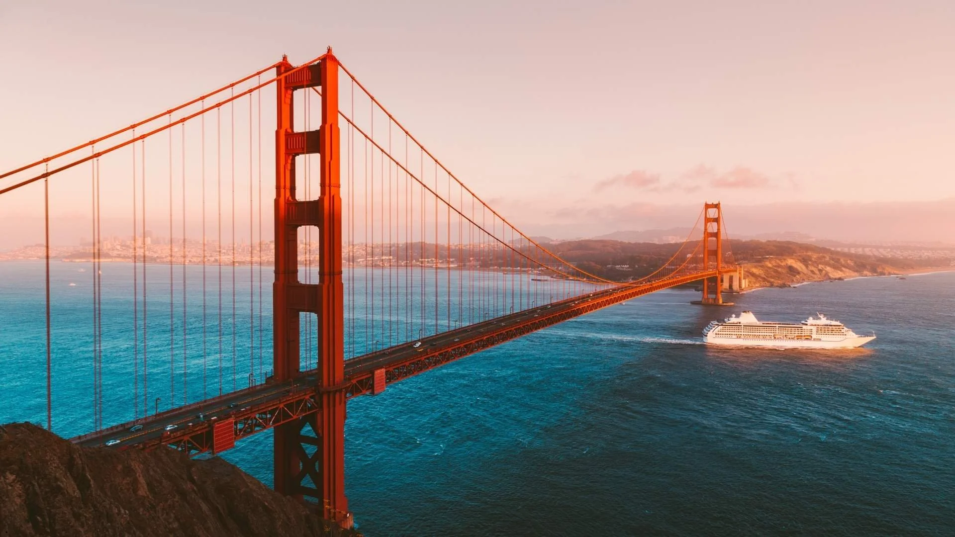 Aerial view of the Golden Gate Bridge at sunset with a cruise ship passing beneath, representing the San Francisco trailer rental starting point for California road trips.