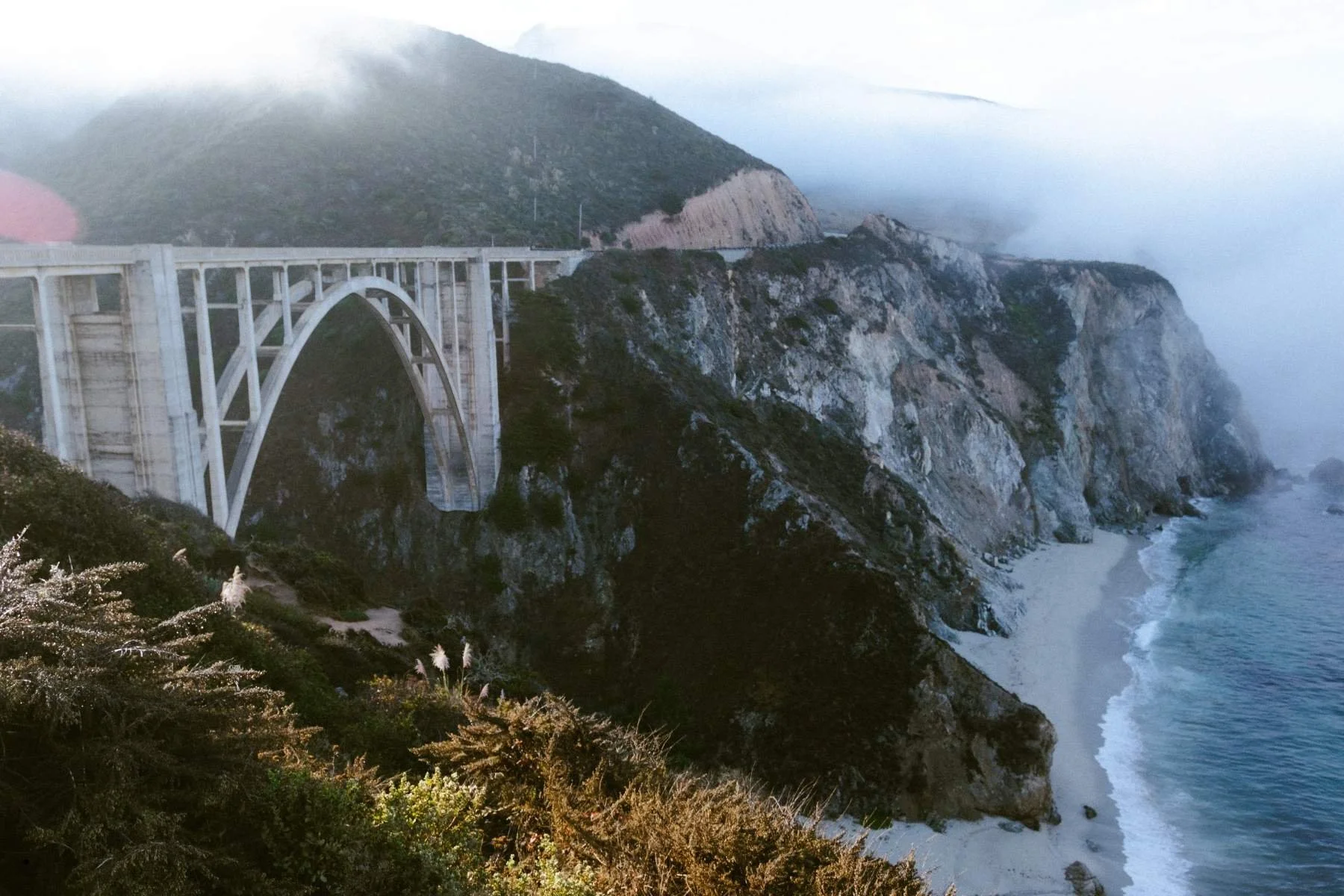 Travel trailer rental road trip stop at Bixby Creek Bridge in Big Sur, California, with dramatic coastal cliffs and Pacific Ocean below