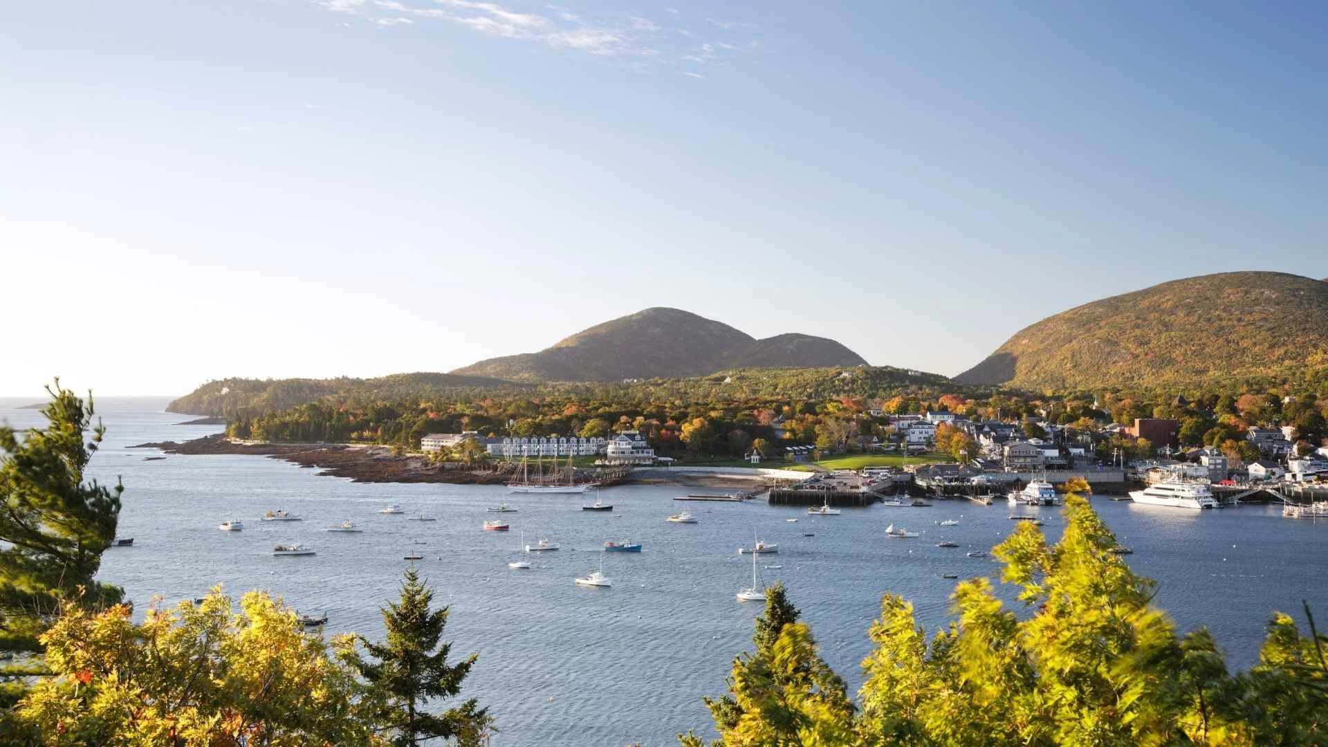 Aerial view of Bar Harbor Maine harbor with sailboats and fishing boats on the water and Acadia National Park hills in the background during fall foliage season