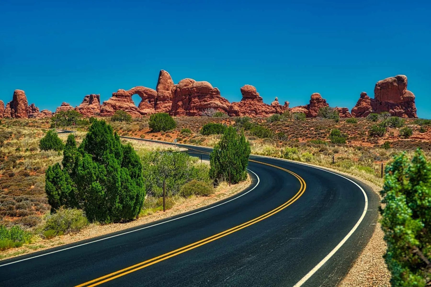 Paved road curving through red rock formations near Arches National Park, a top destination for Utah travel trailer rental trips