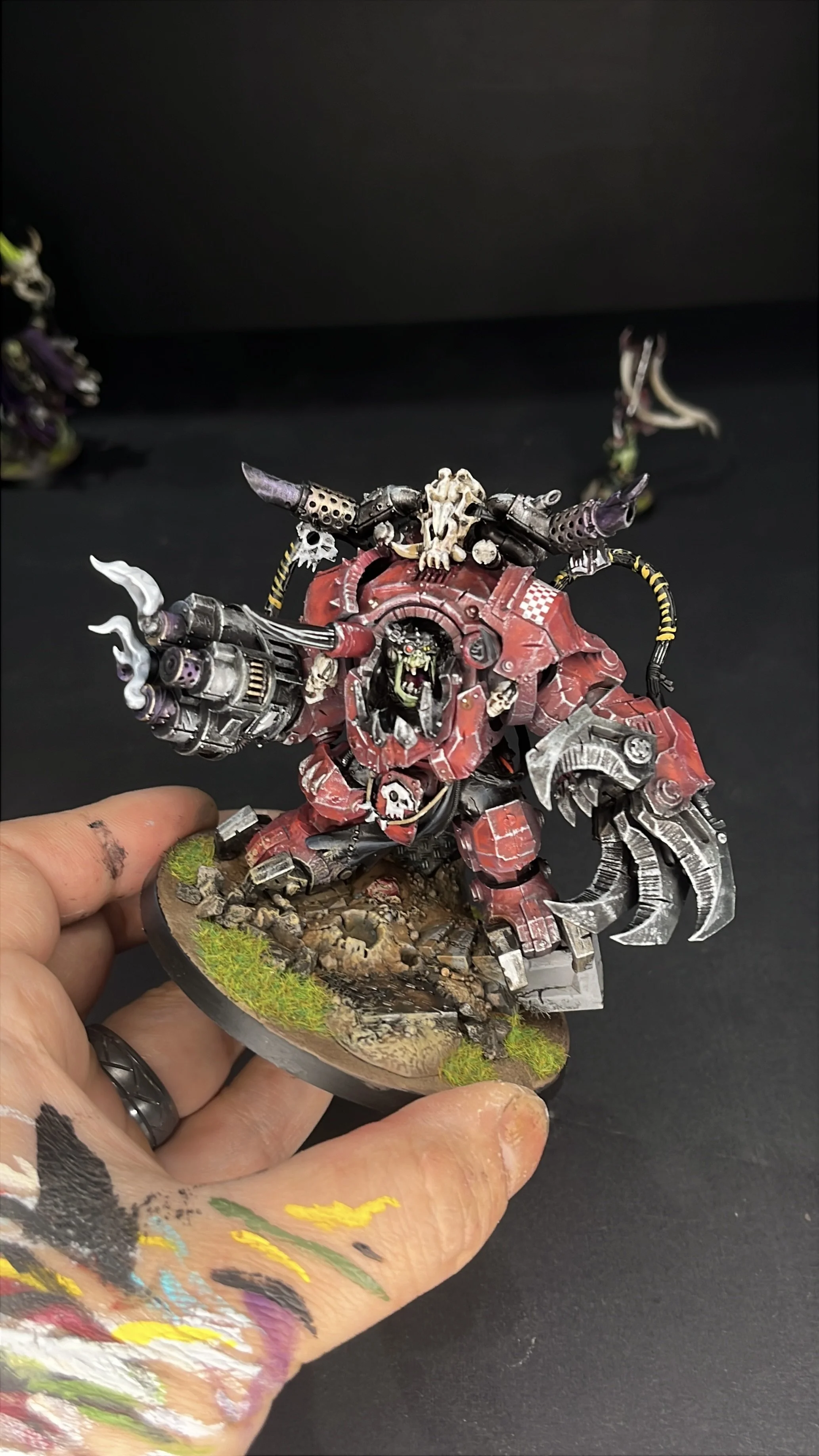 A painted miniature model of a Warhammer 40k chaos space marine in heavy armor, wielding a large claw-like weapon, with skull and mechanical details, mounted on a detailed base with grass and rocks.