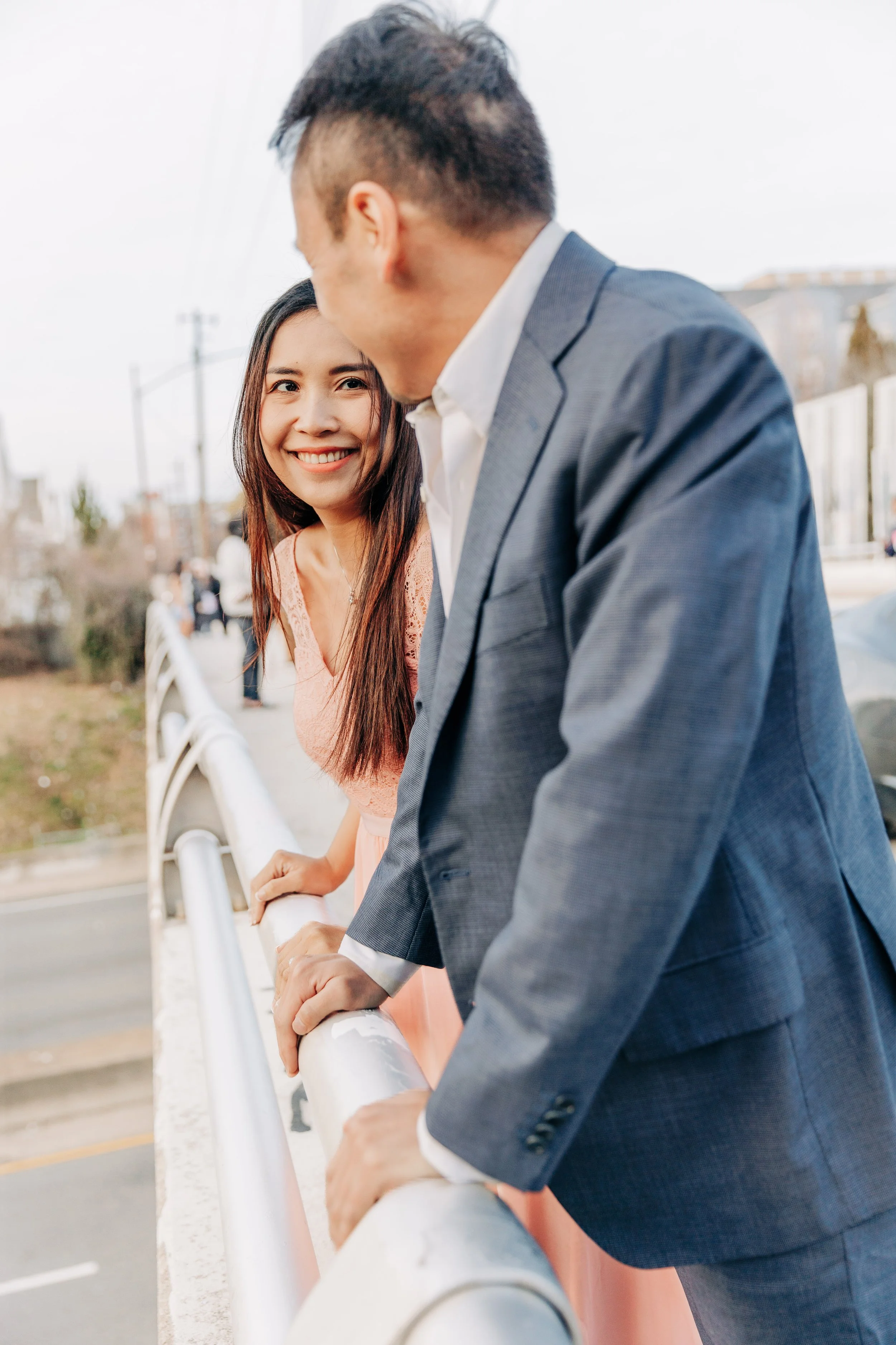 A woman in a pink dress smiling at a man in a suit on a bridge