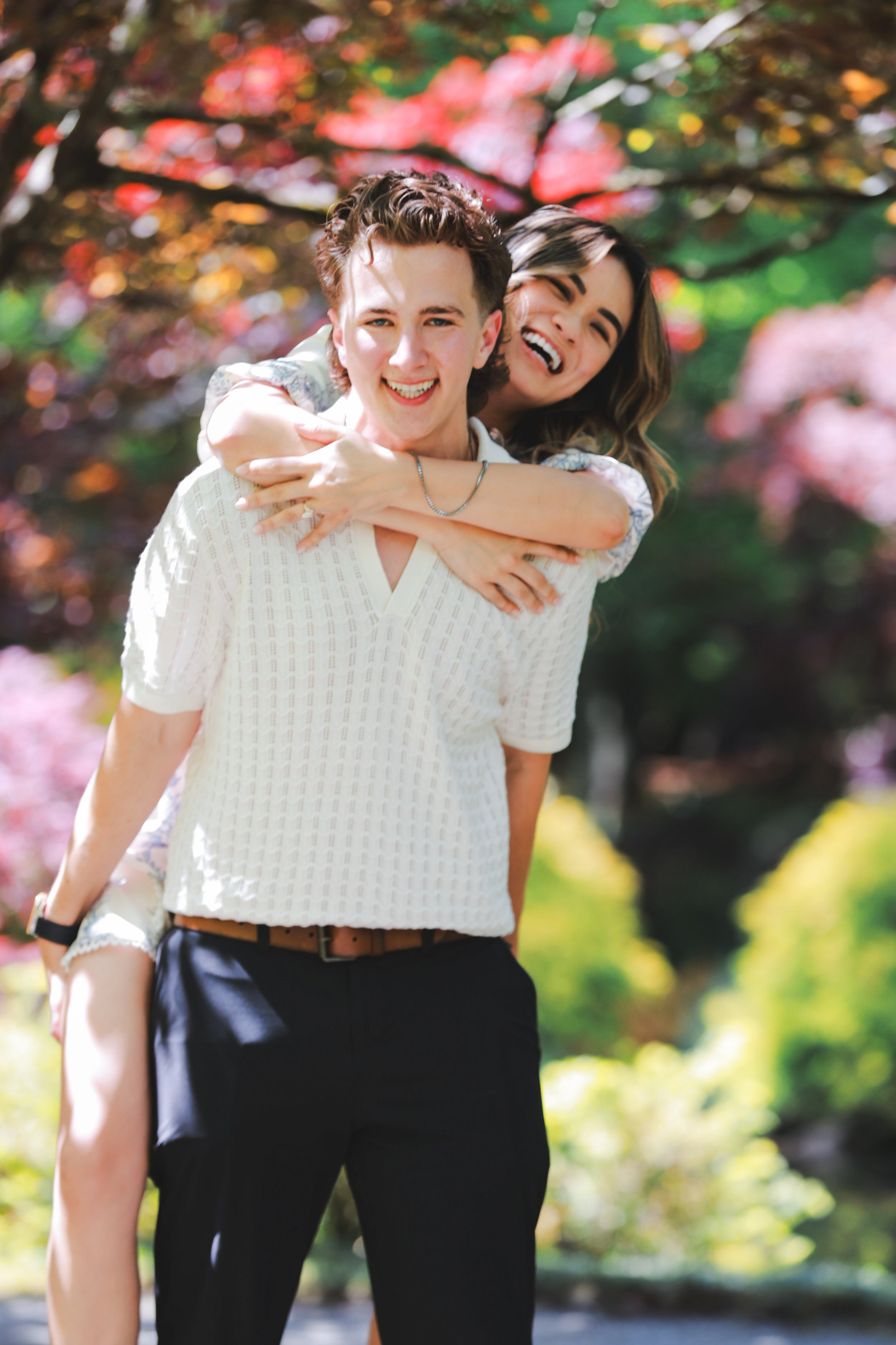 Two young adults, a man and a woman, laughing and enjoying each other outdoors in a park with colorful autumn trees.