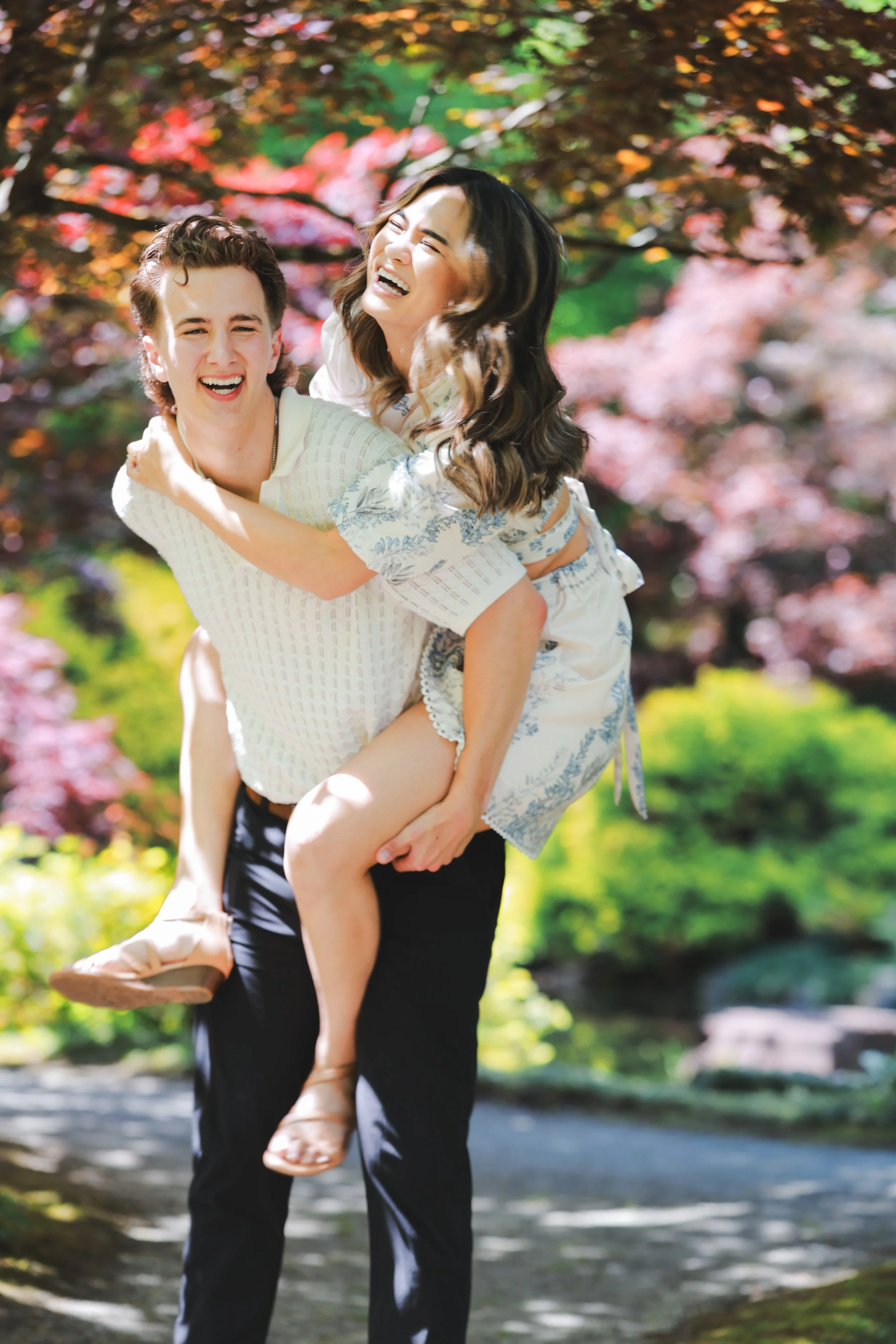 Man carrying woman on his back in a park with trees and colorful leaves.