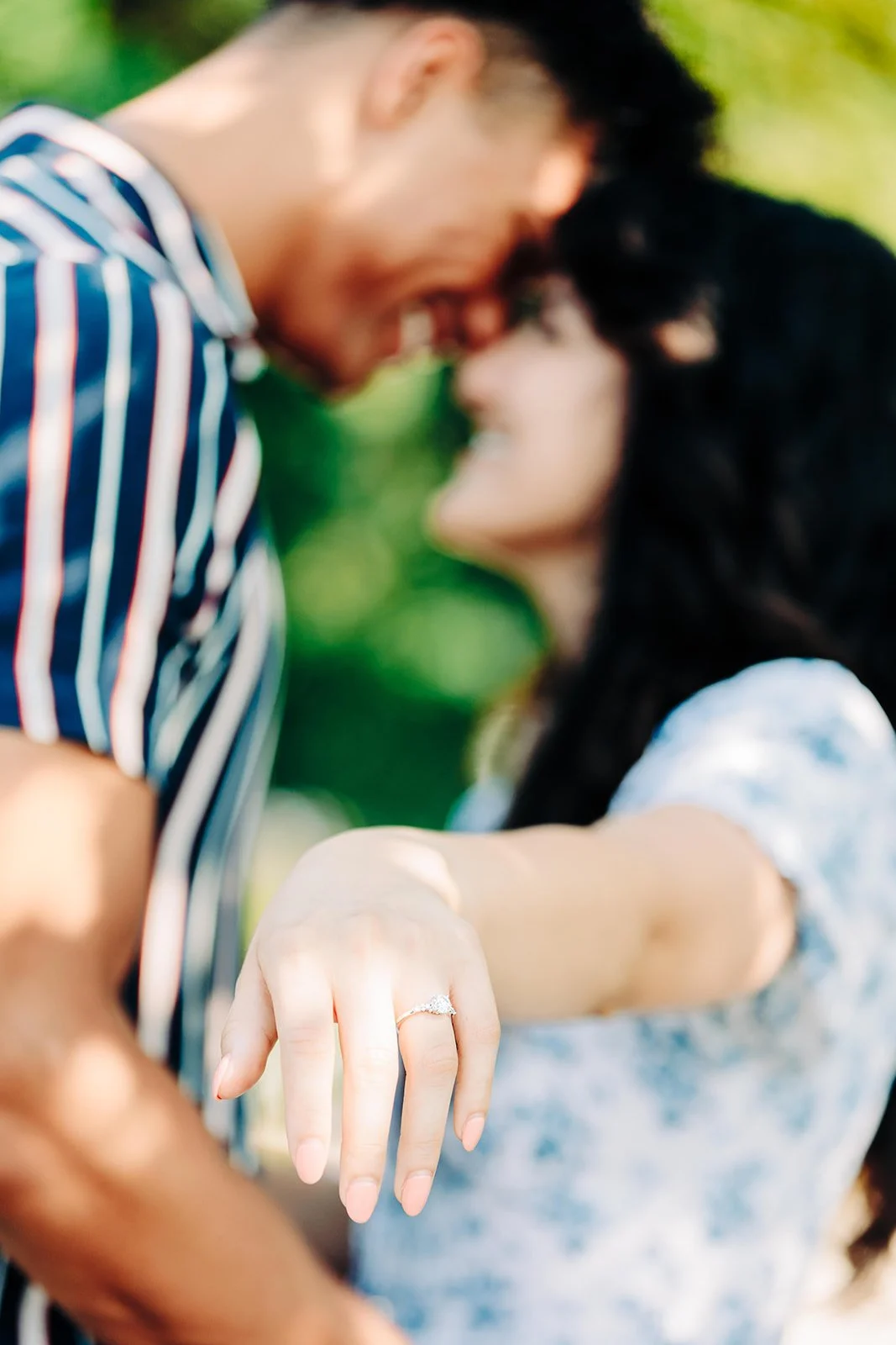 A couple touching foreheads, with a focus on the woman's hand displaying an engagement ring.