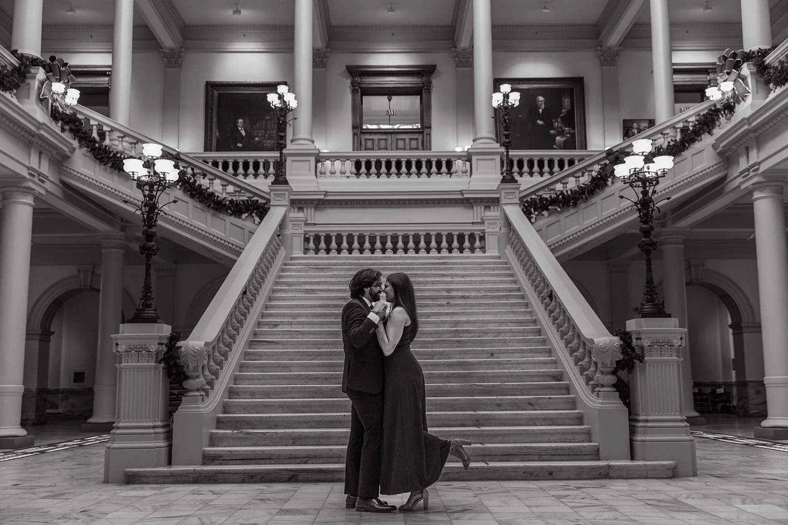 A romantic couple dancing on a grand staircase inside a historic building, decorated with garlands and ornate lamps.
