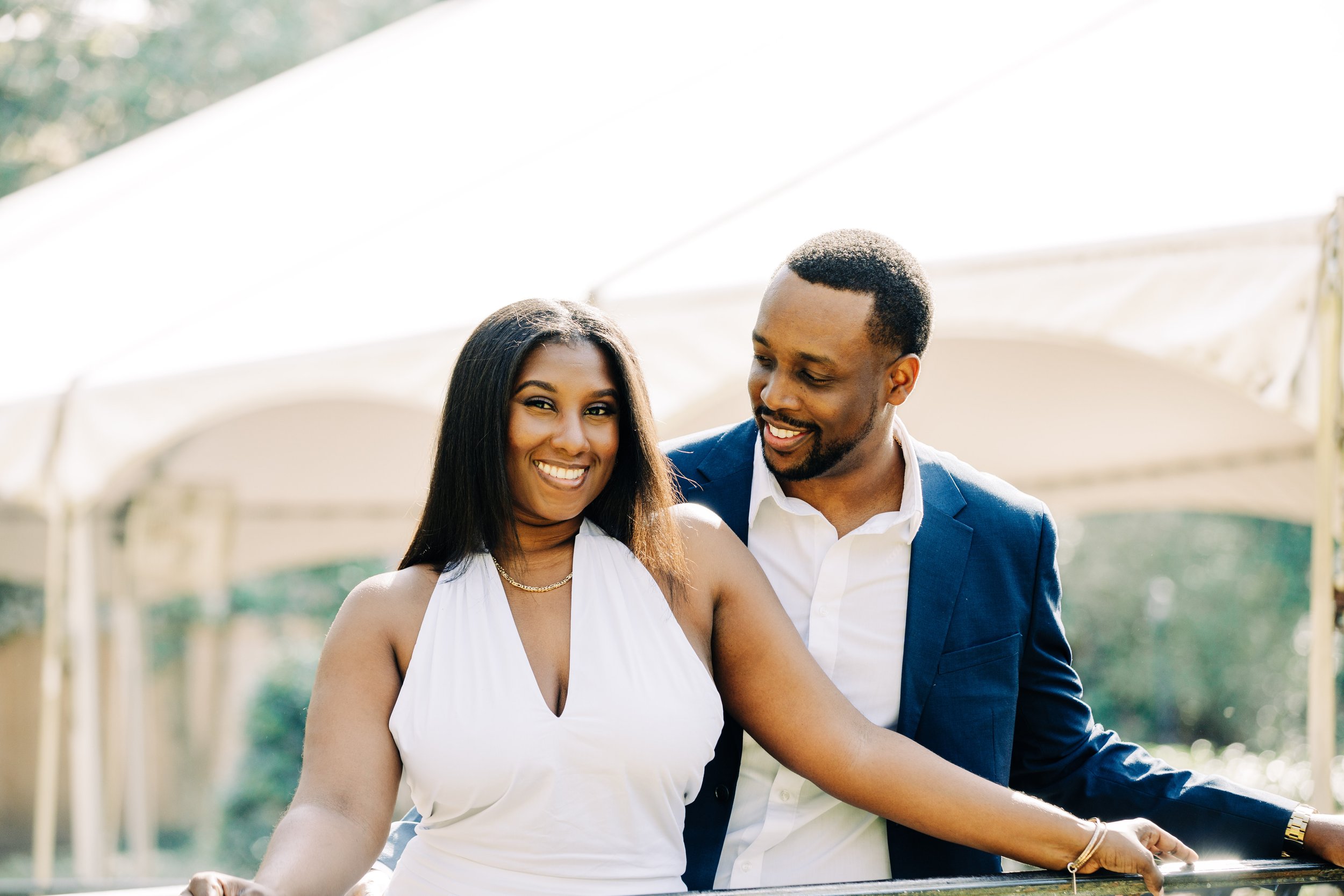 A smiling woman in a white dress and a man in a blue suit are enjoying a moment together outdoors.