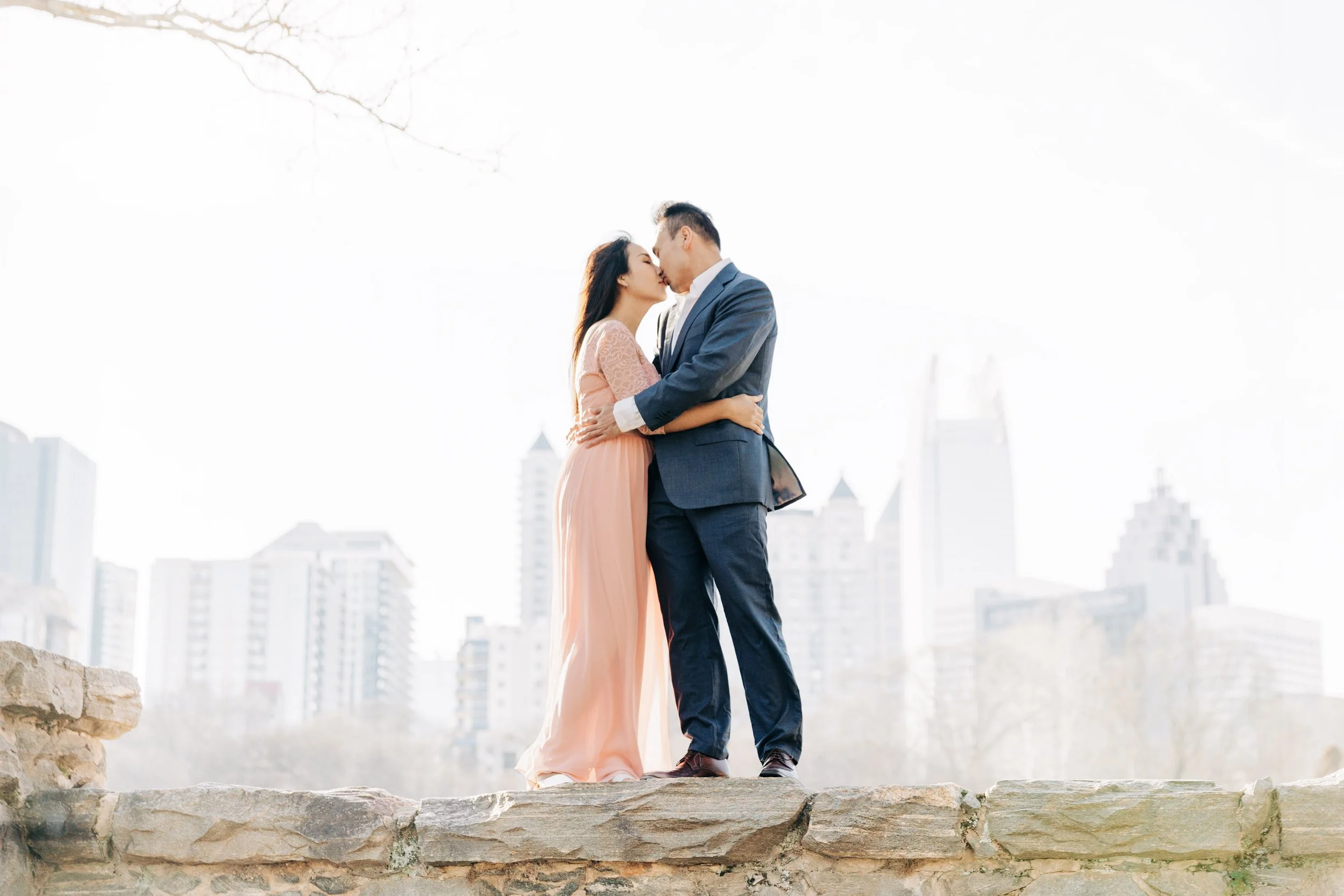 A young couple sharing an intimate moment outdoors during autumn, with the tall young man kissing the forehead of the young woman who is smiling with her eyes closed.