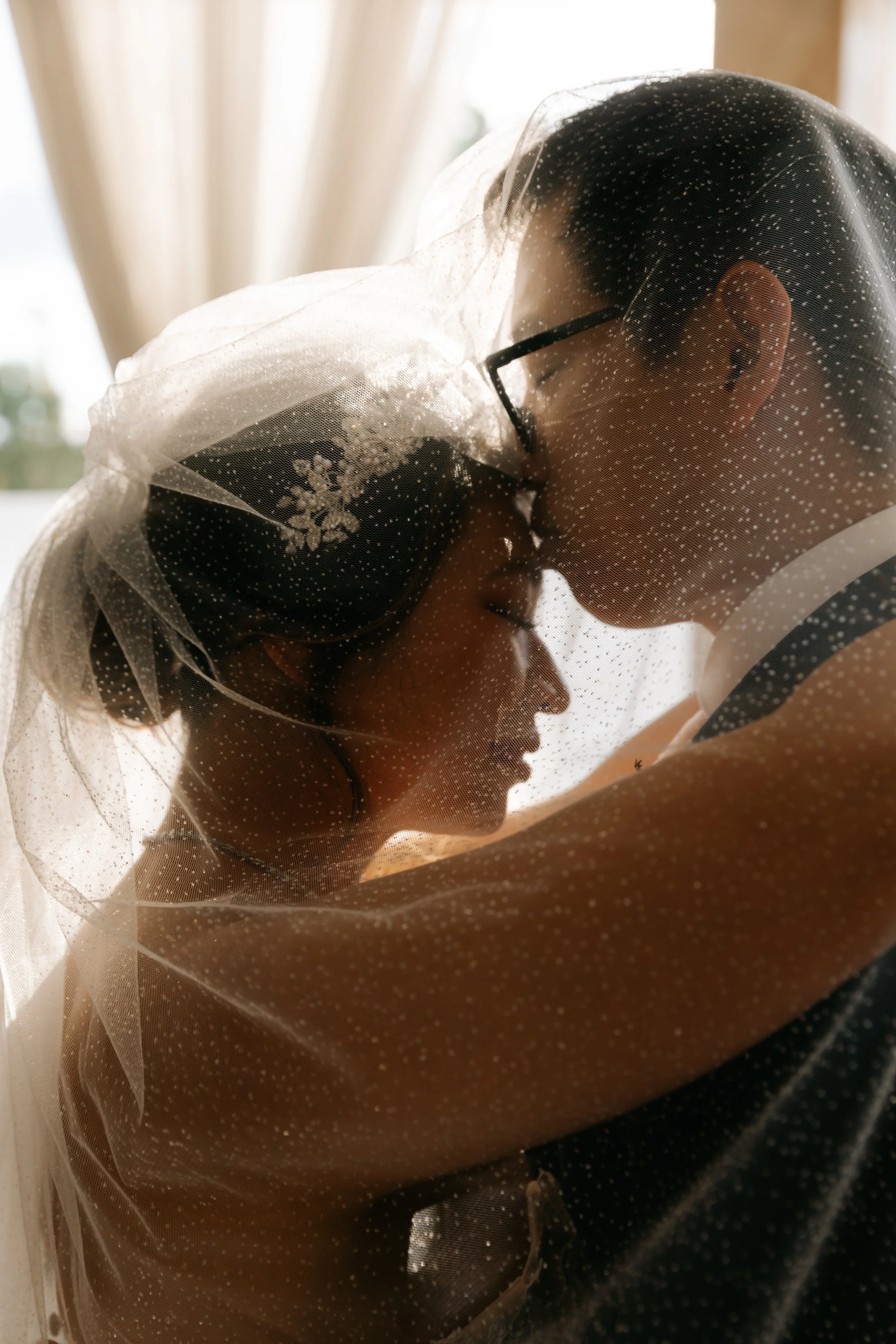 A bride and groom kissing, with a sheer veil covering their faces, in a close-up shot.