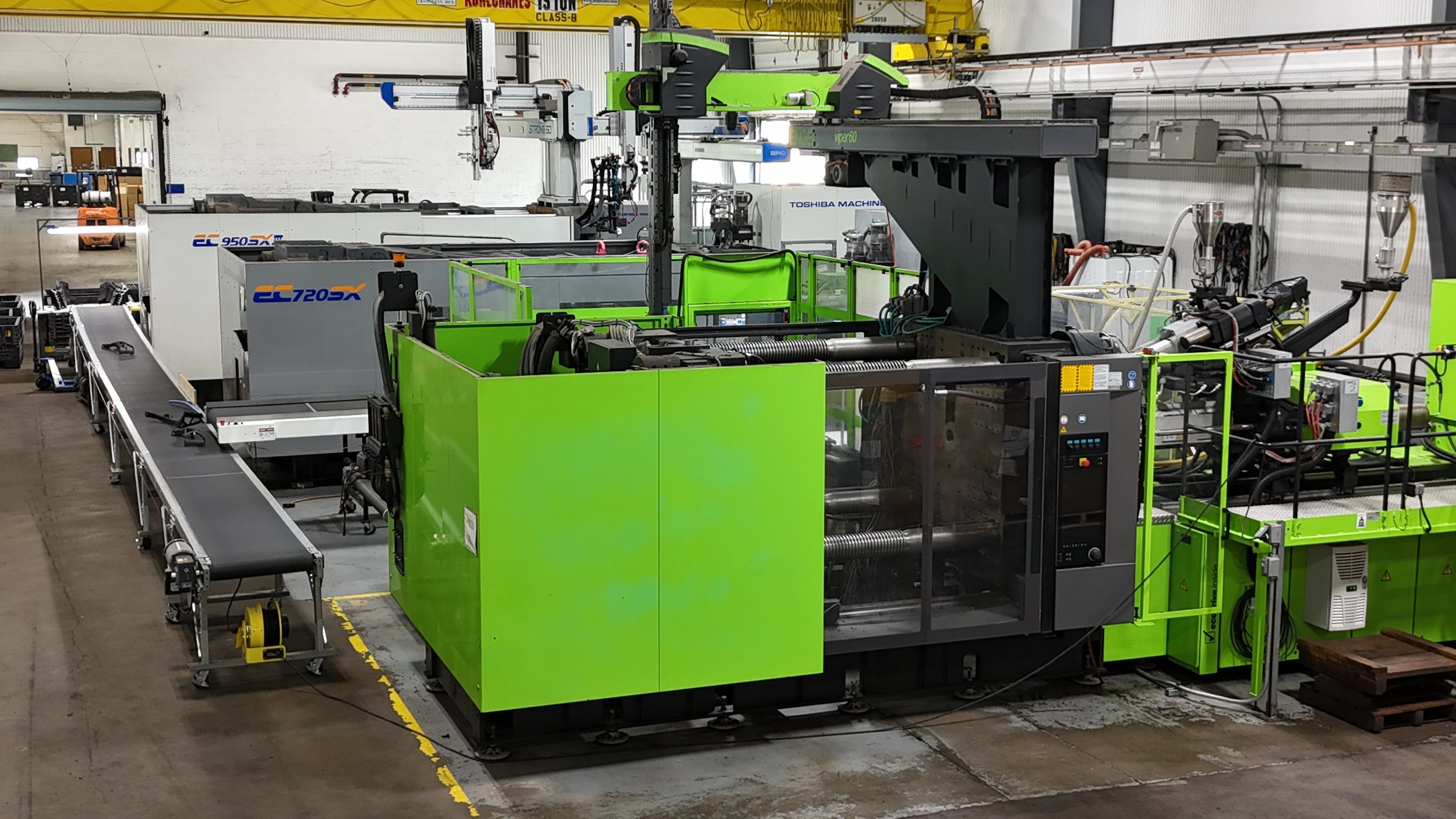 Multiple Large Engel and Toshiba Injection Molding Machines, green and black machinery in a factory setting with conveyor belts, control panels, and robotic arms.