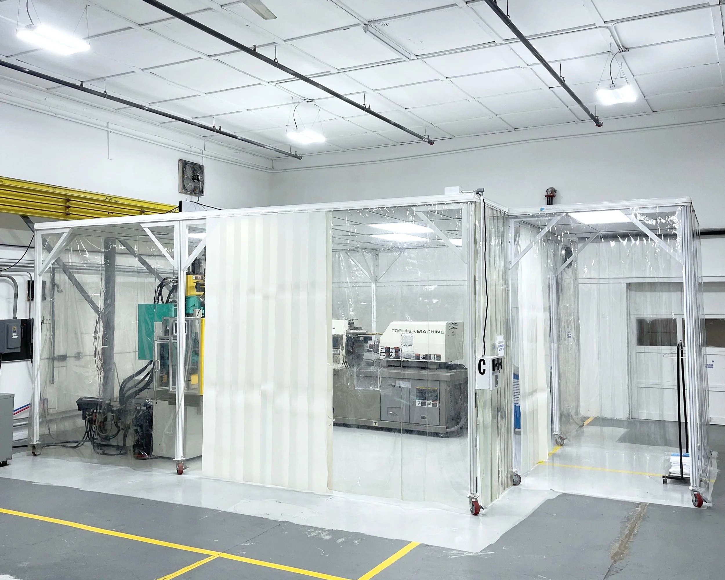 ISO Class 7 Cleanroom with transparent plastic enclosure and Injection Molding Machinery inside, in a well-lit warehouse or manufacturing facility.