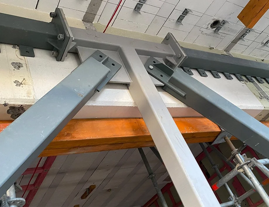 Seismic Engineering - Strata Group Engineers NZ | Construction site with steel beams and supports, showing a metal framework secured with bolts, surrounded by concrete and wooden elements.