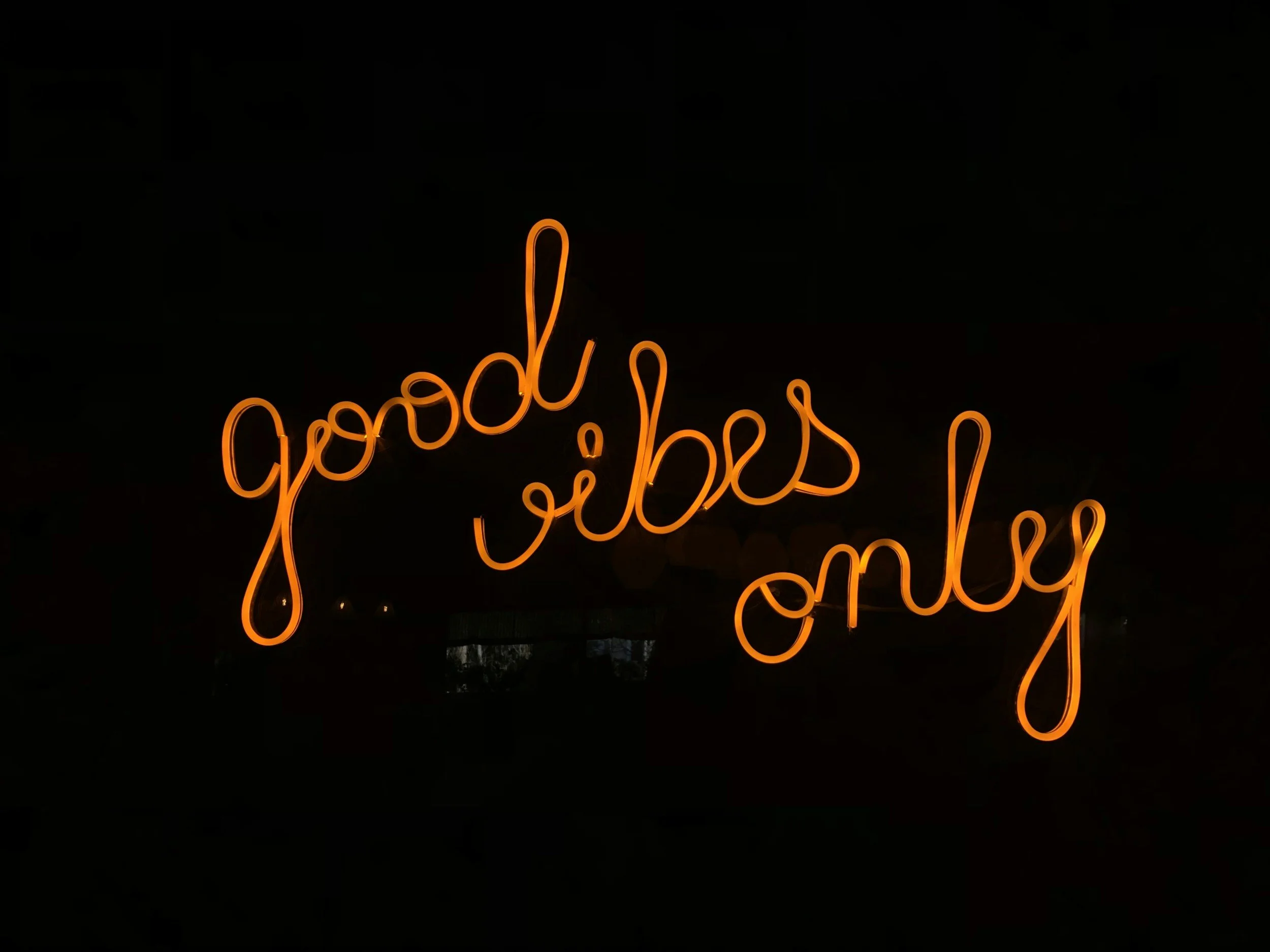 Neon sign with orange cursive text reading 'good vibes only' against a black background.