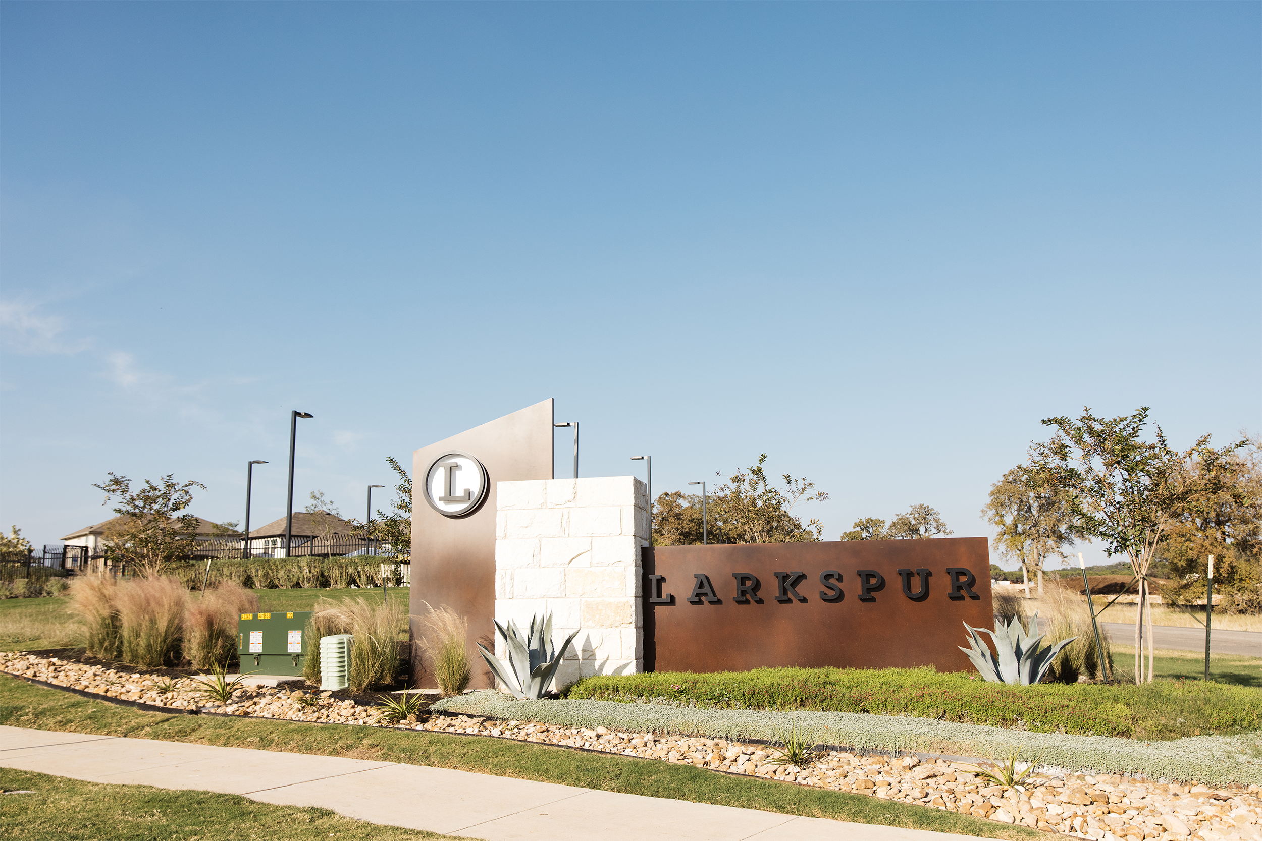 Entrance sign for Larkspur residential community with decorative landscaping and plants under a clear blue sky.