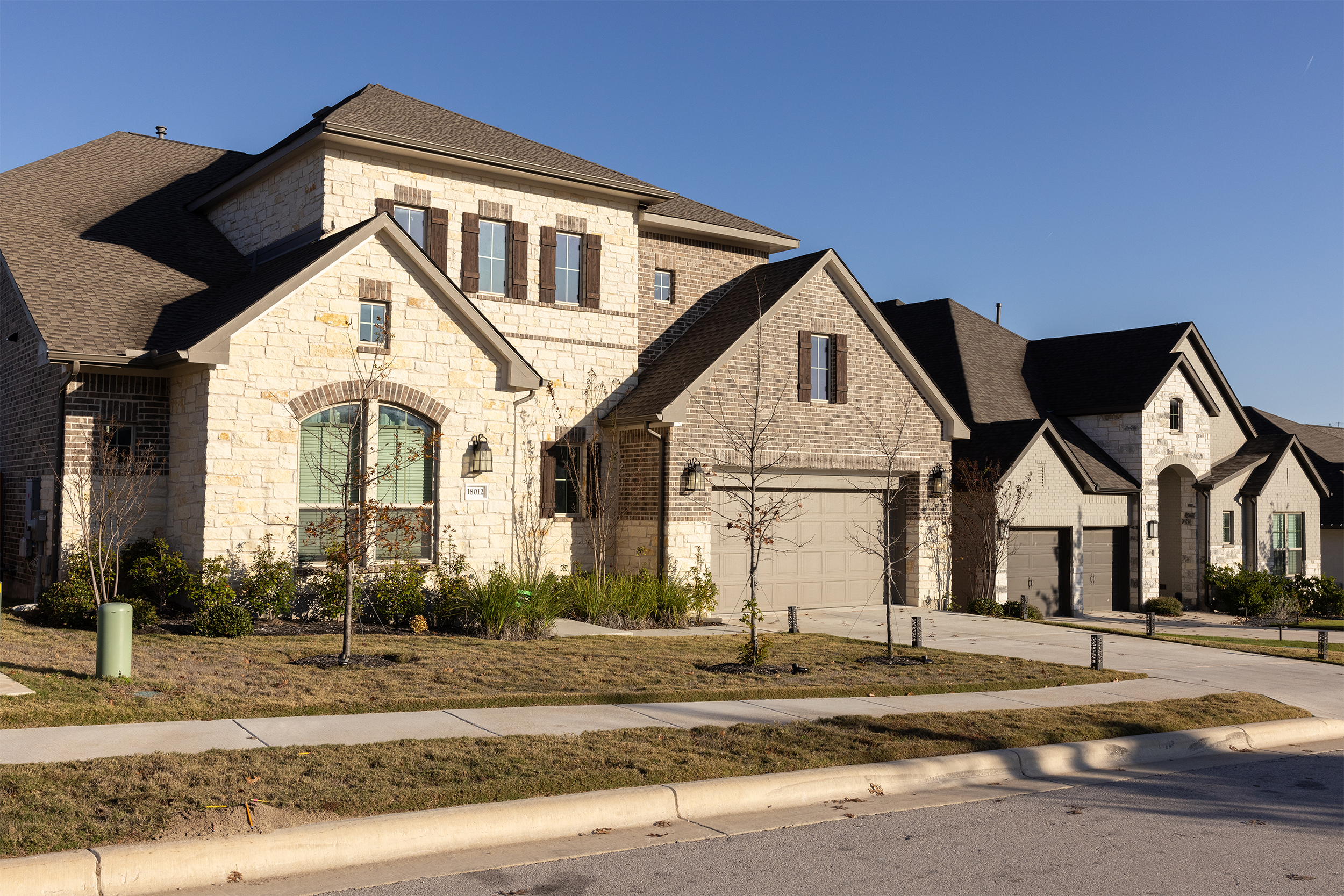 Row of suburban stone and brick houses with manicured lawns and clear blue sky