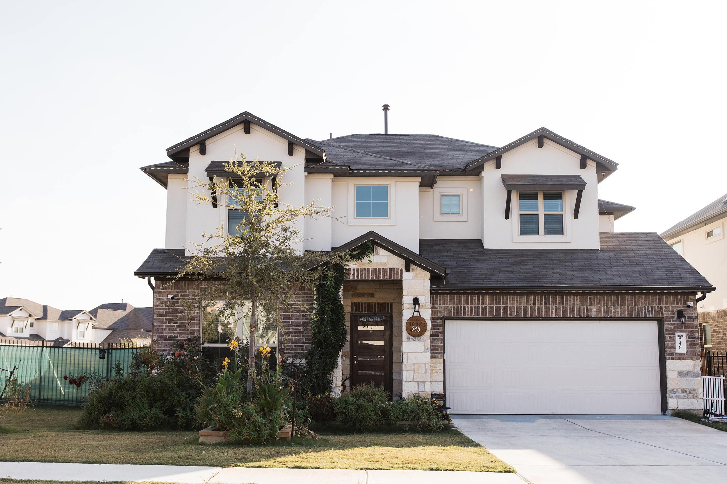 Modern two-story house with a brick and stucco exterior, large windows, and a landscaped front yard.