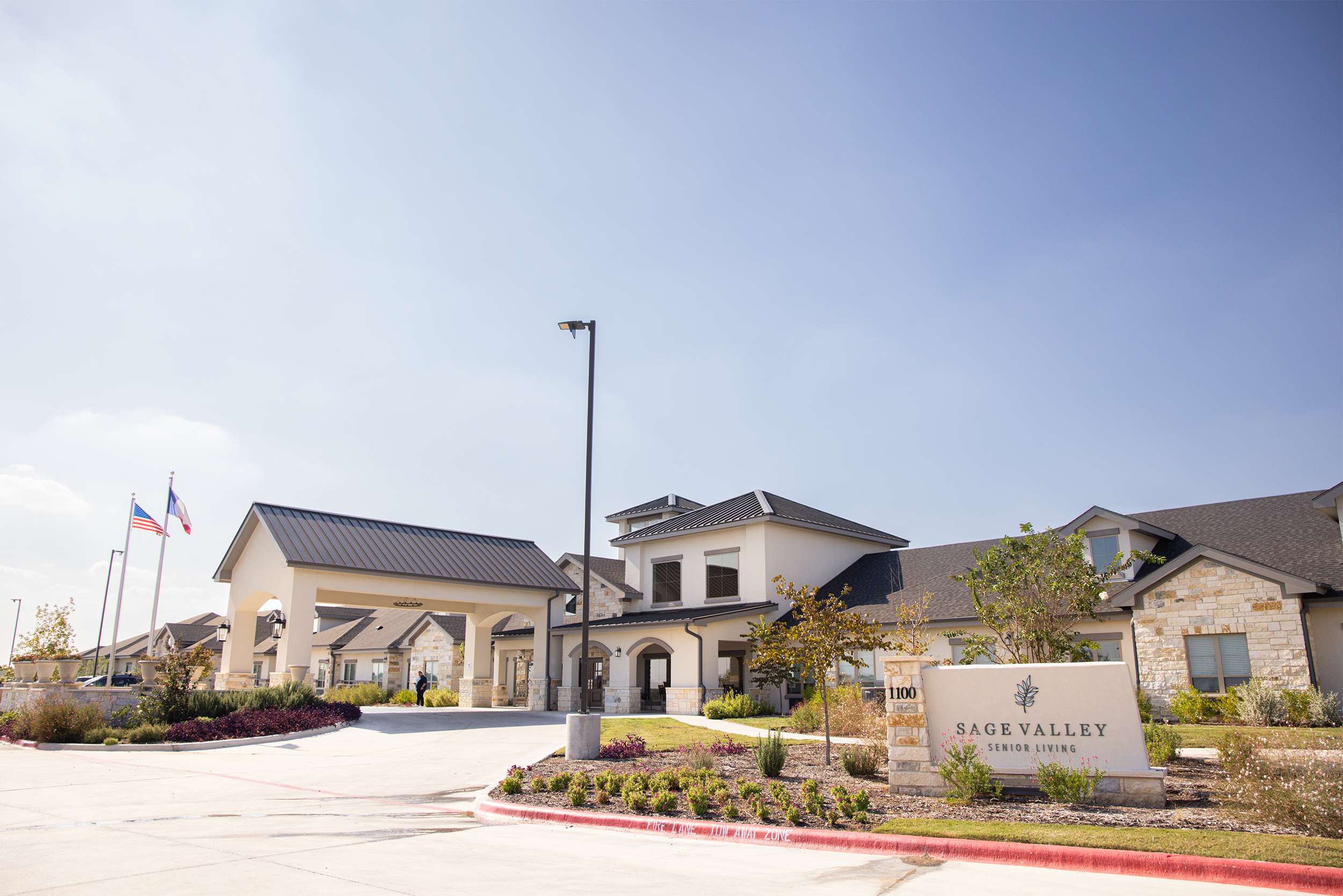 Sage Valley Senior Living building with flags and landscaping under a blue sky.