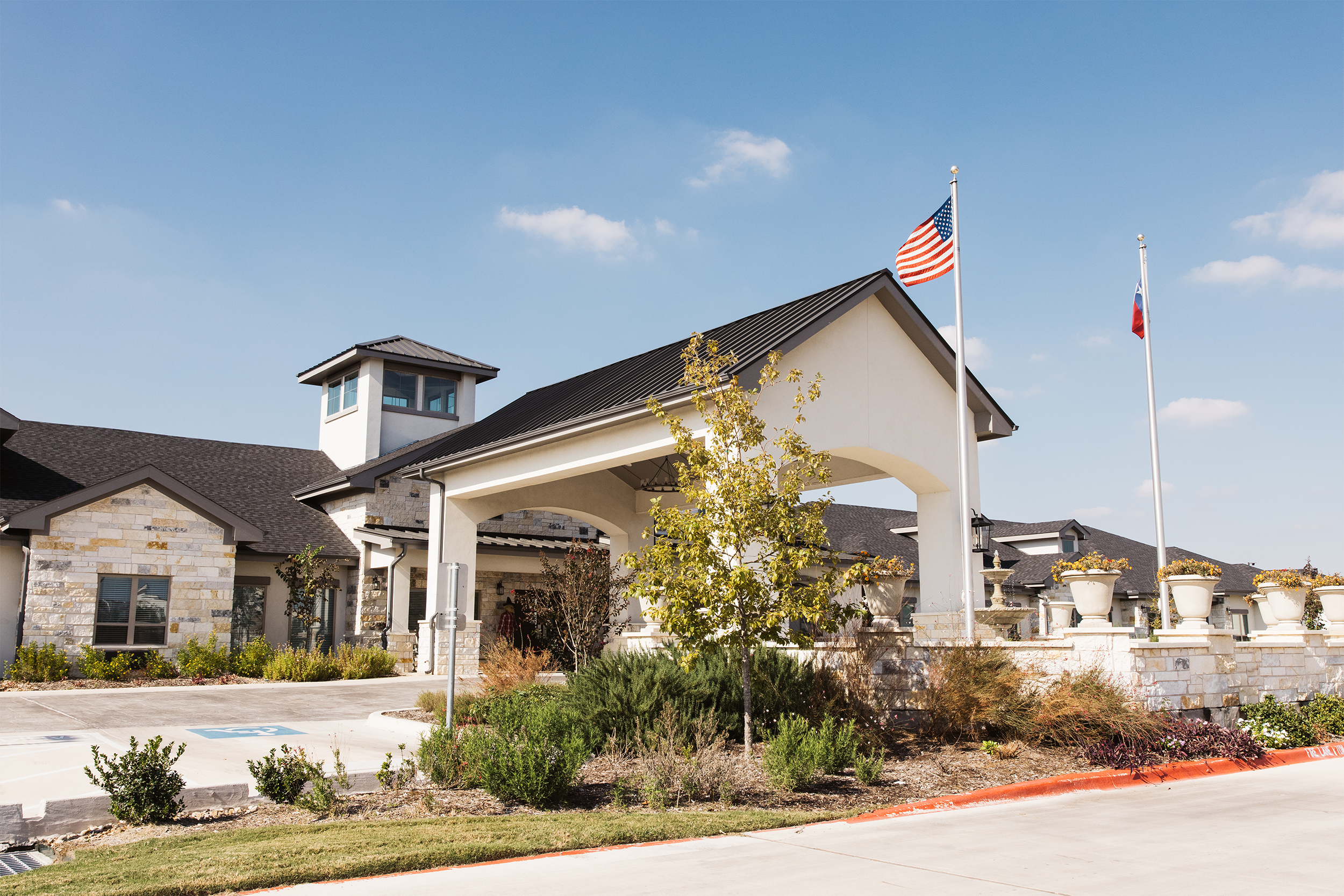Exterior view of a building with a peaked roof, American and Texas flags, and landscaped garden area