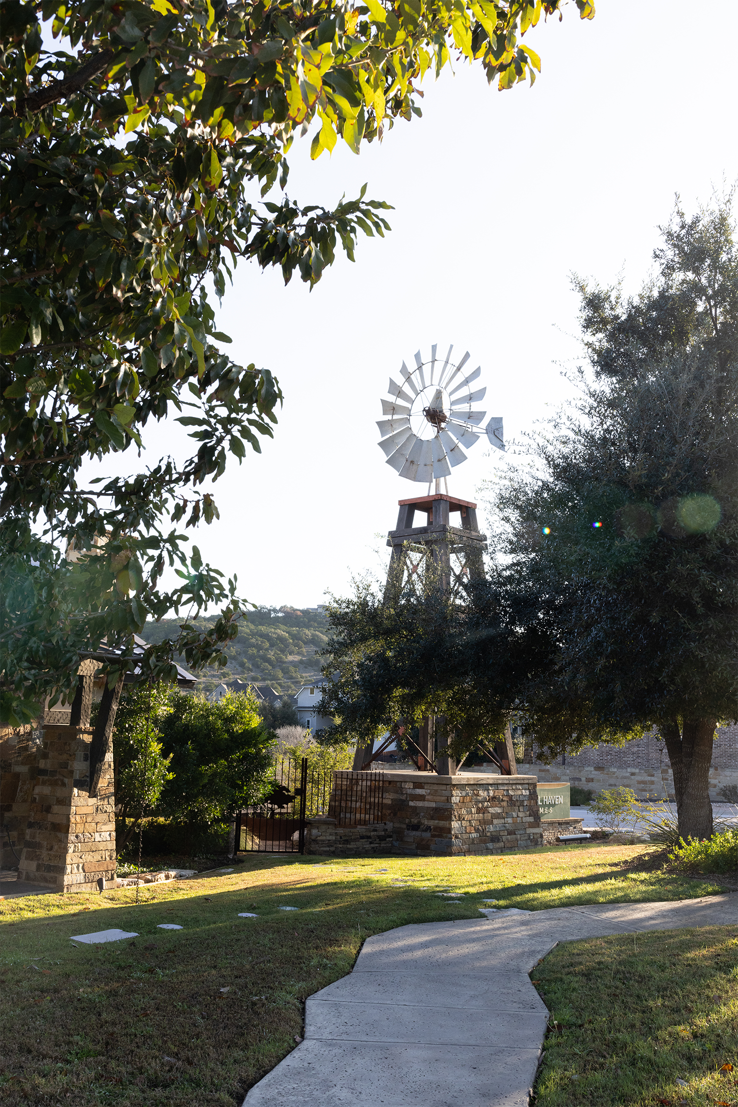 Outdoor scene with a windmill, trees, and a winding path leading through grassy area.