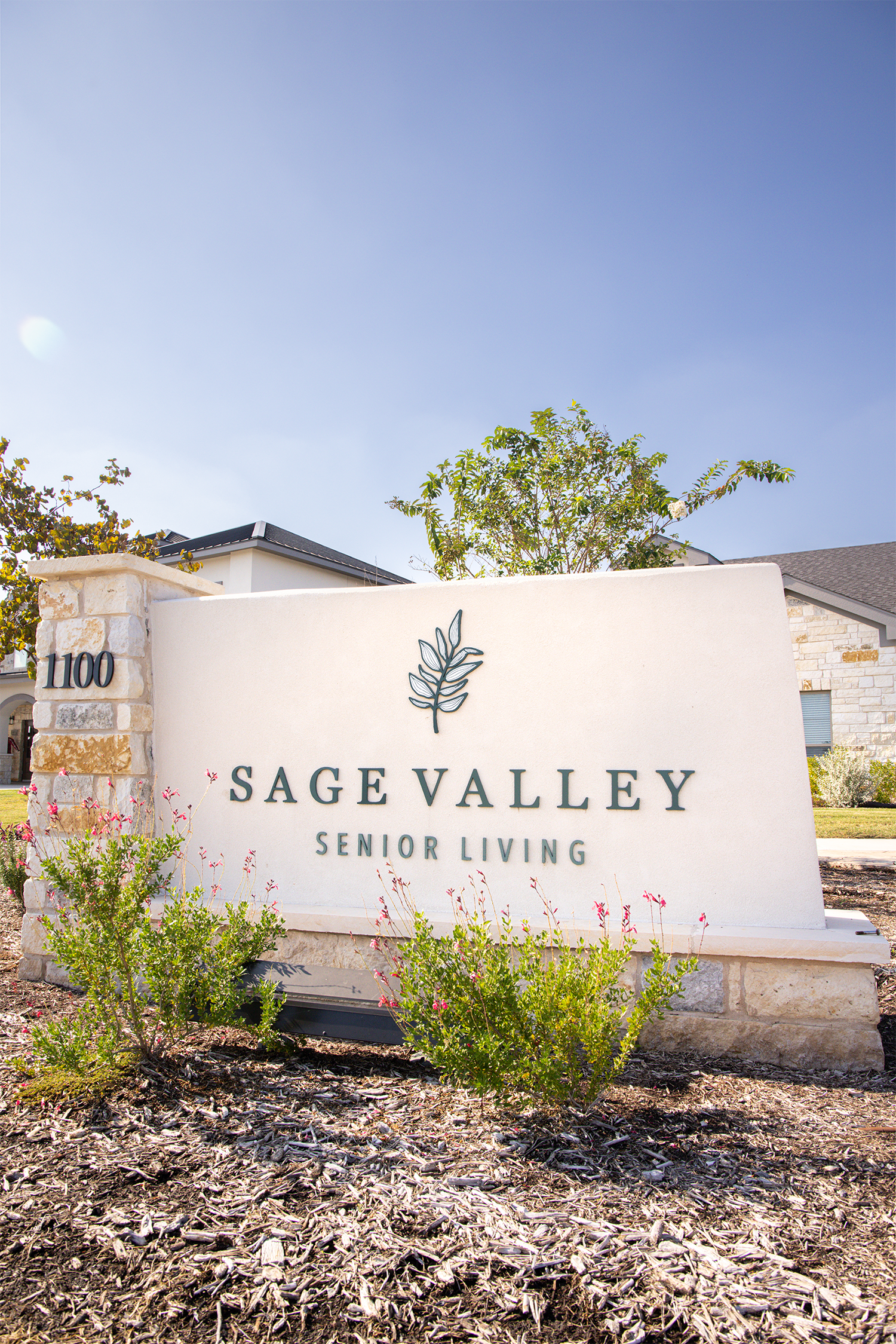 Entrance sign for Sage Valley Senior Living against a clear blue sky with surrounding plants and stone elements.