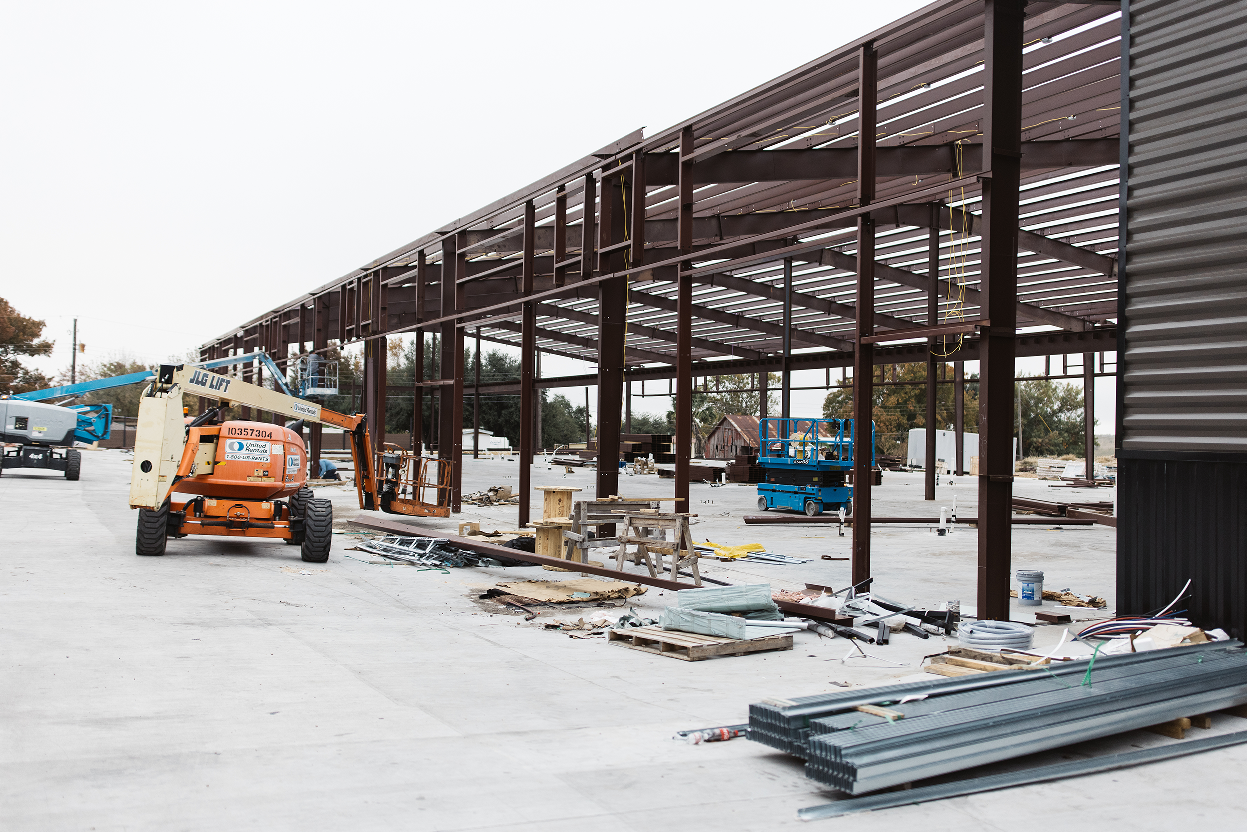Construction site with steel frame structure, lift equipment, and building materials.