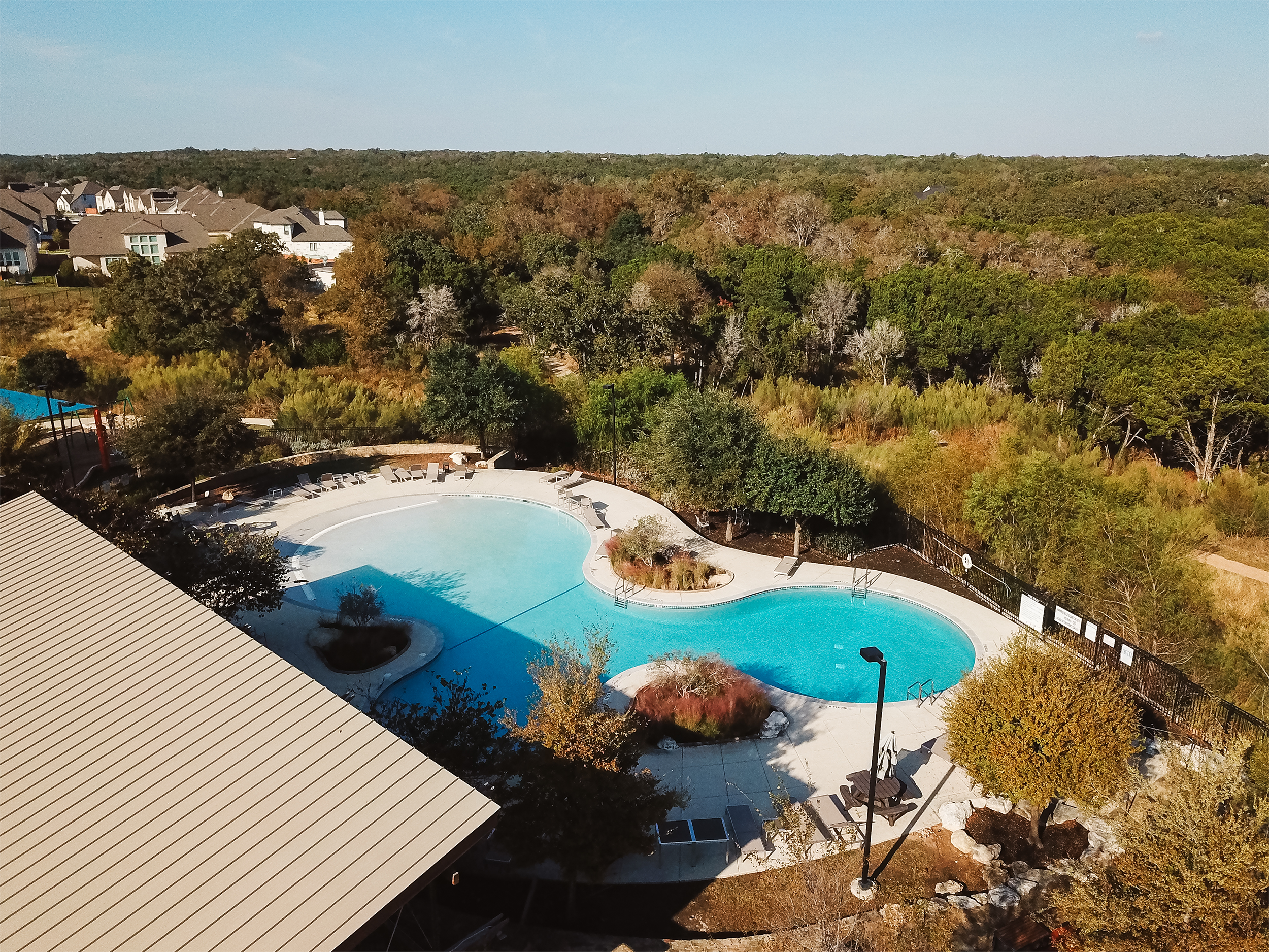 Aerial view of a swimming pool surrounded by trees and residential buildings.